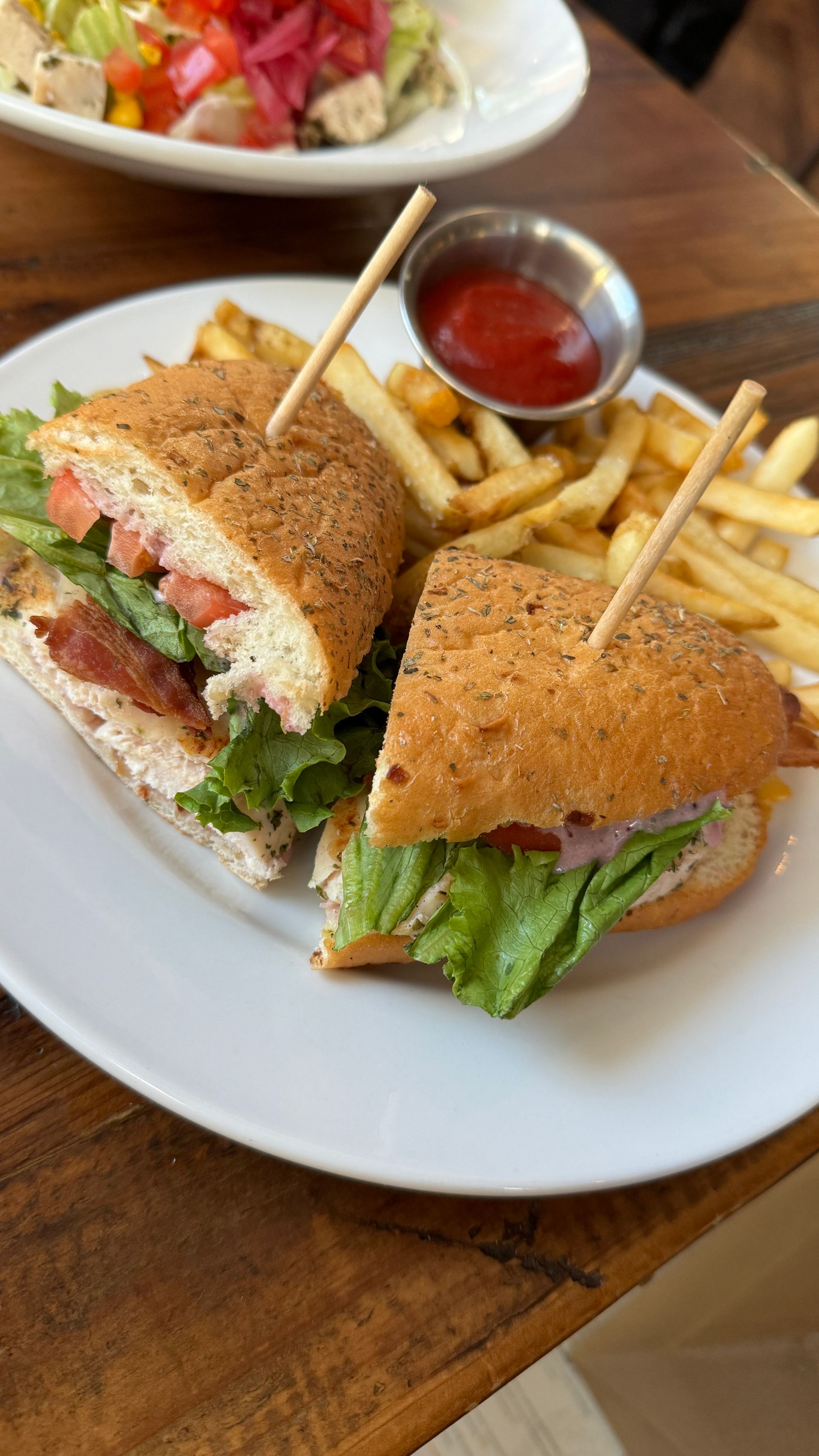 A sandwich and french fries on a white plate on a wooden table.