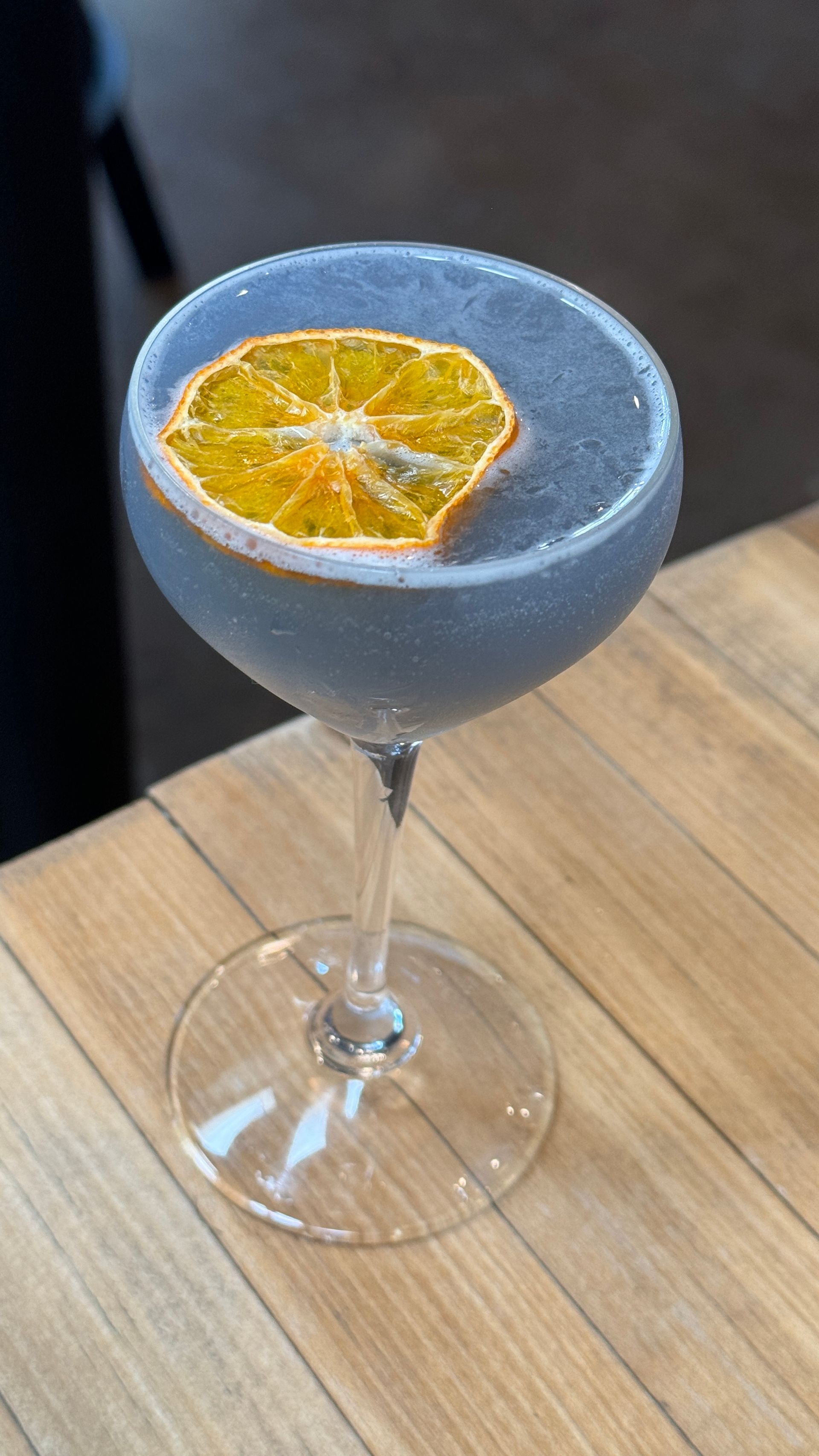 A blue cocktail with an orange slice on top is sitting on a wooden table.