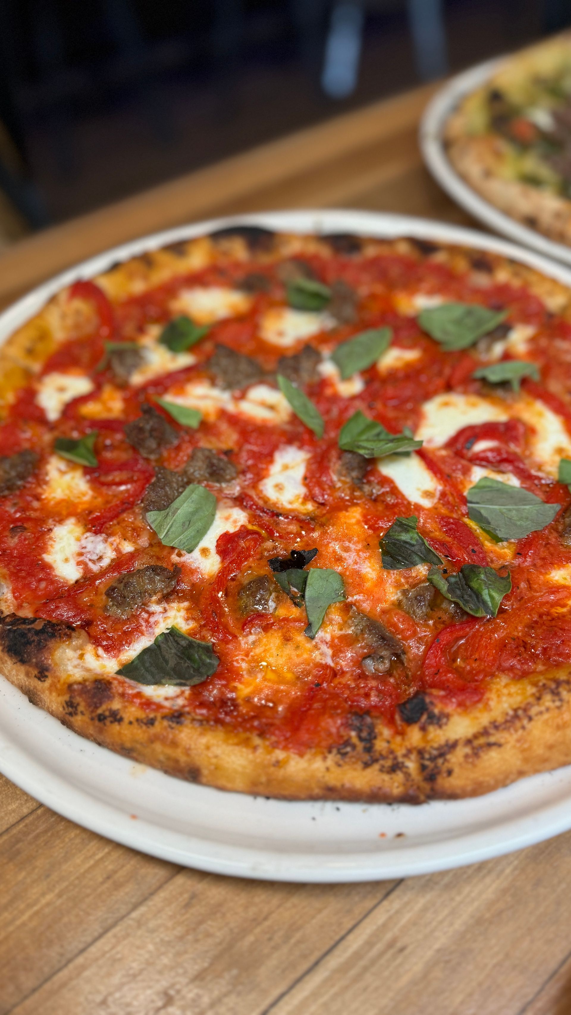A pizza is sitting on a white plate on a wooden table.