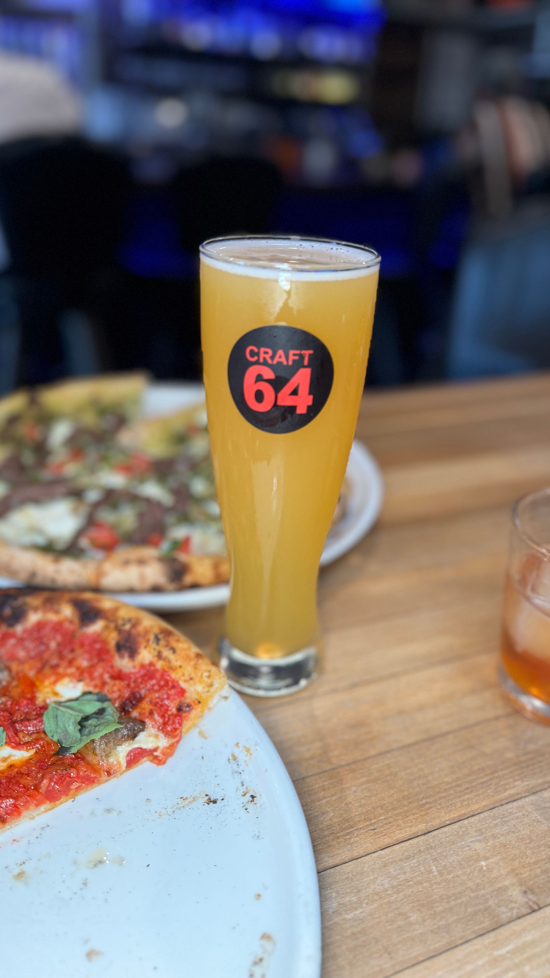 A glass of beer is sitting on a table next to a pizza.