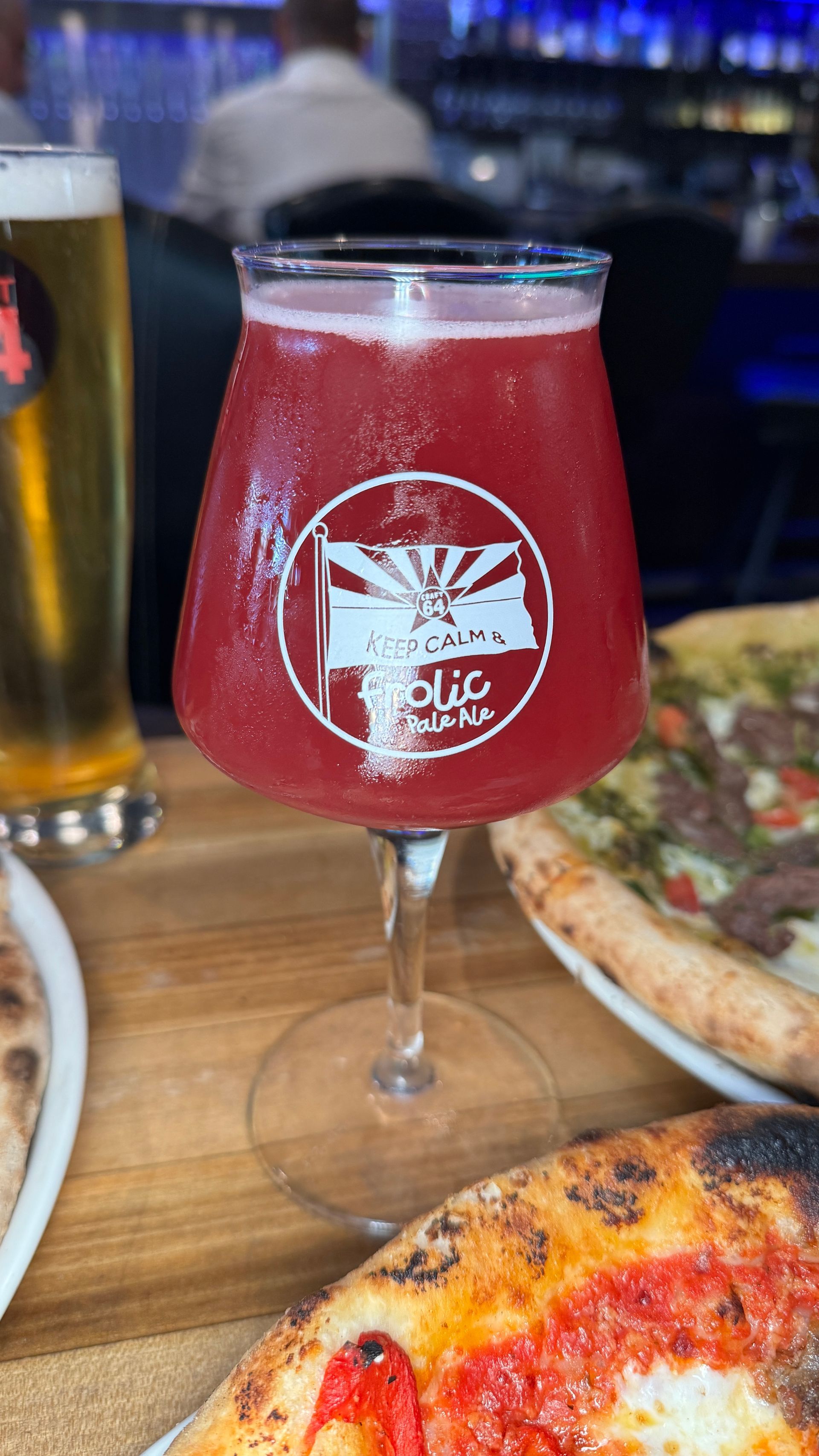 A glass of red liquid is sitting on a table next to pizza.