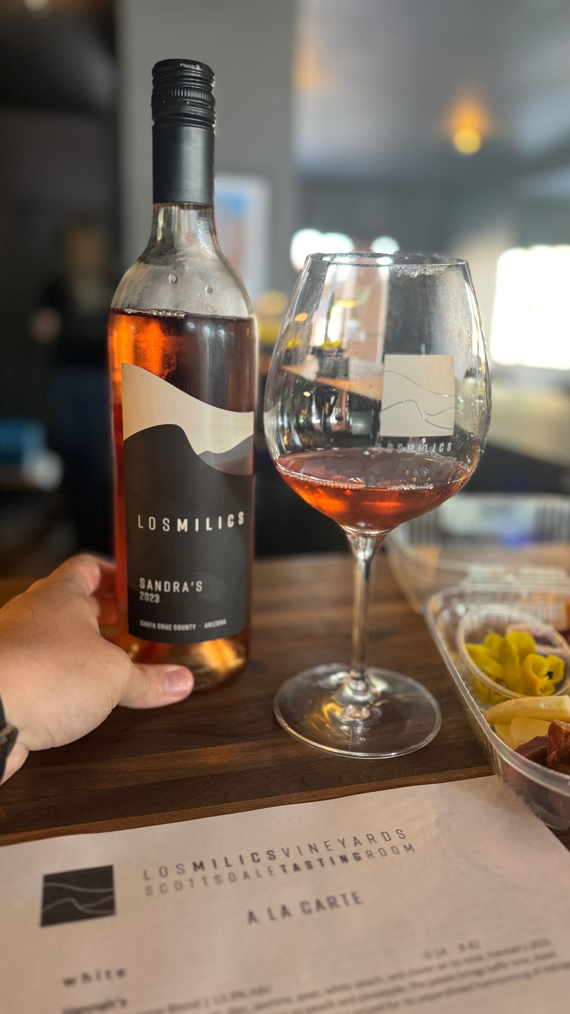 A person is holding a bottle of wine and a glass of wine on a table.