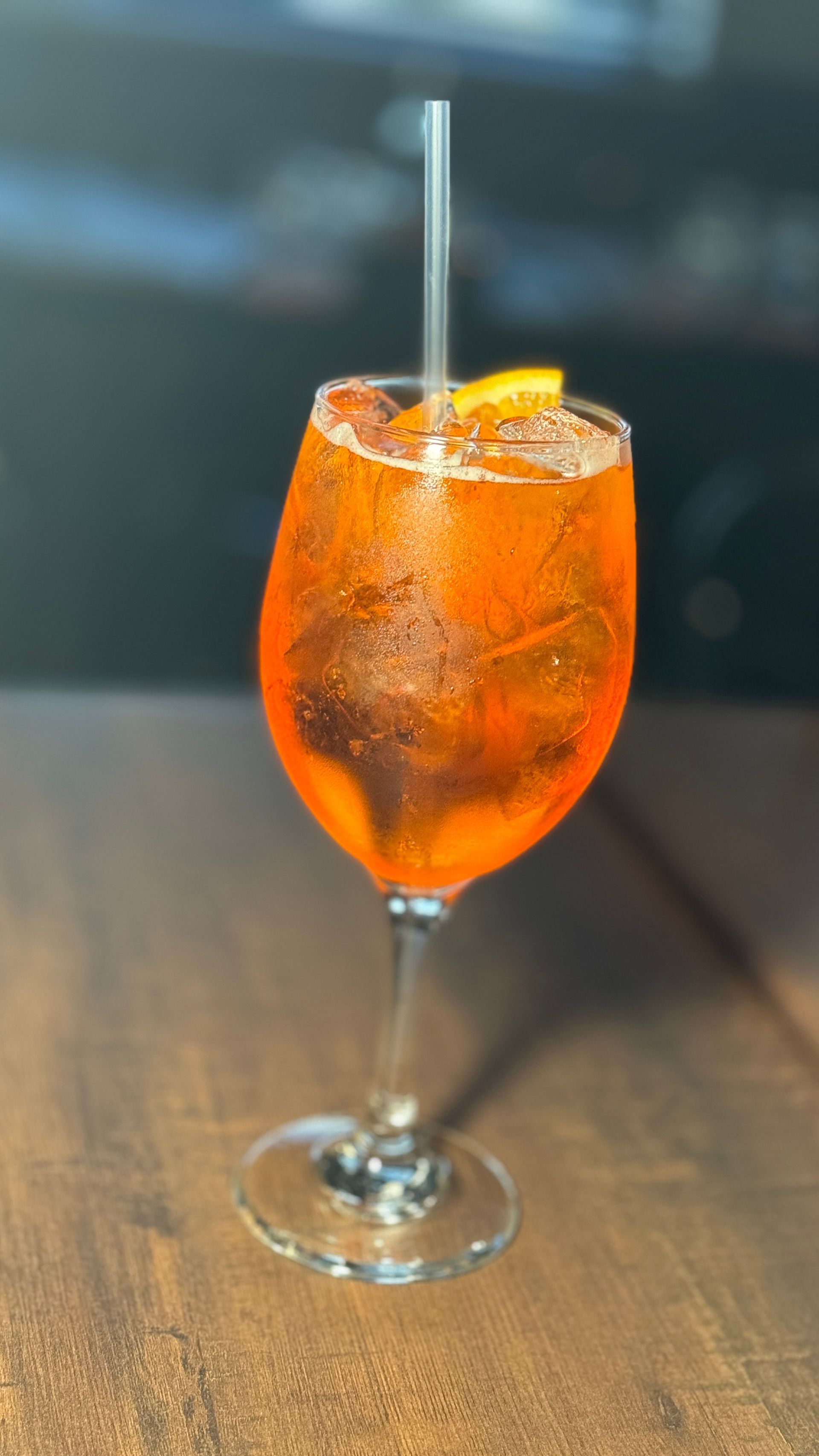 A glass of orange juice with a straw on a wooden table.