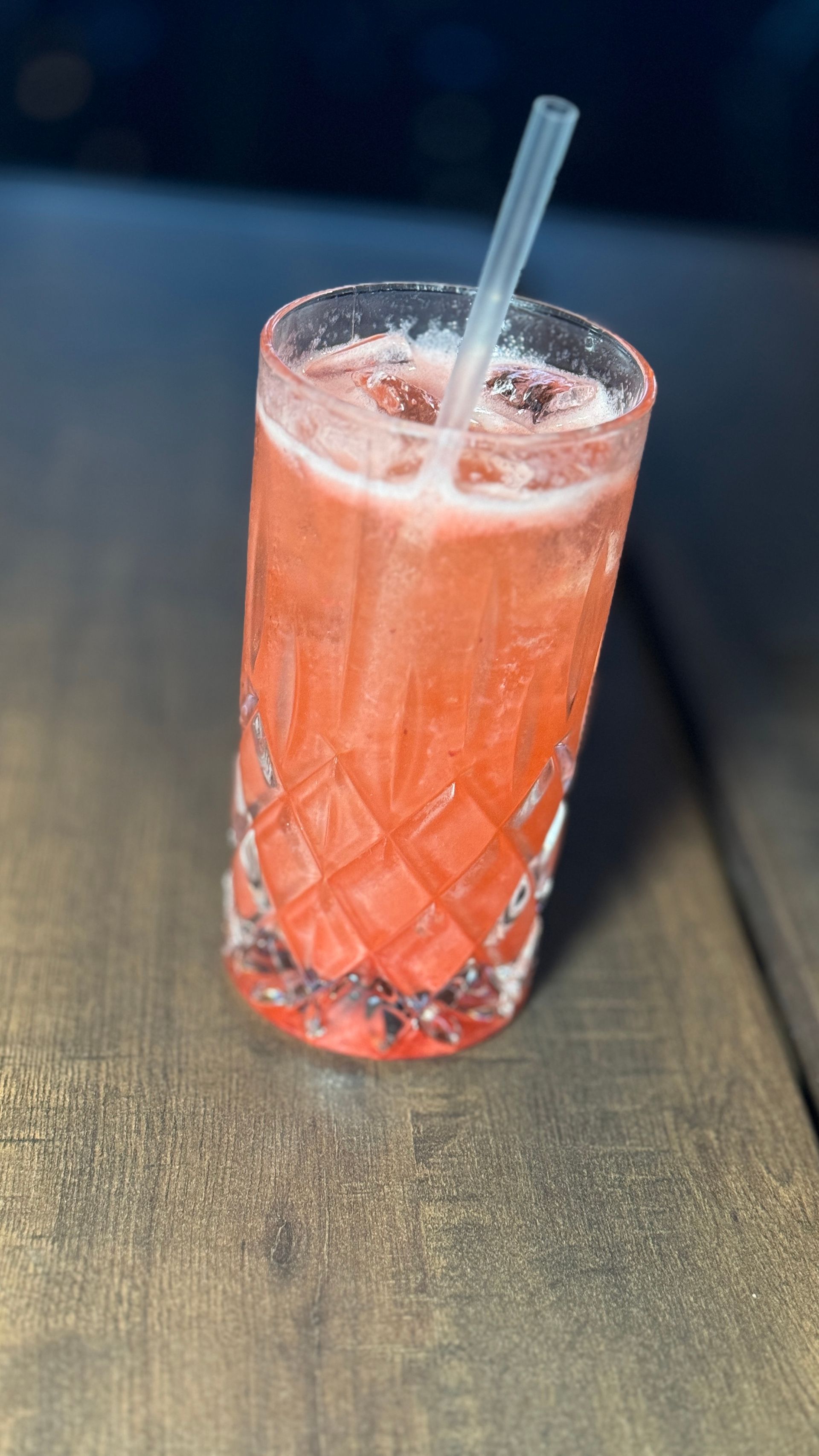 A glass of pink liquid with a straw in it on a table.