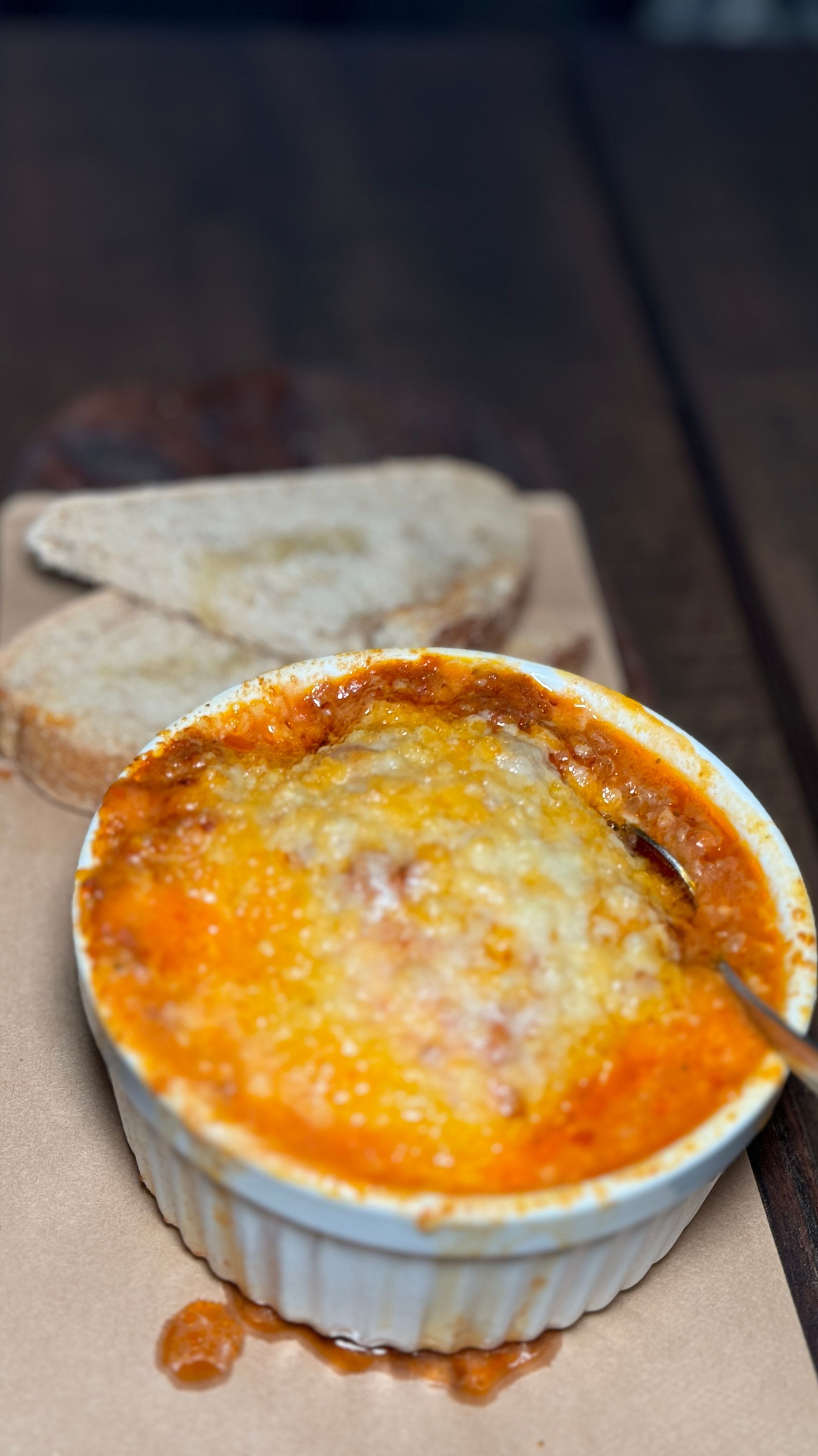 A bowl of food with a spoon in it is on a table next to a piece of bread.