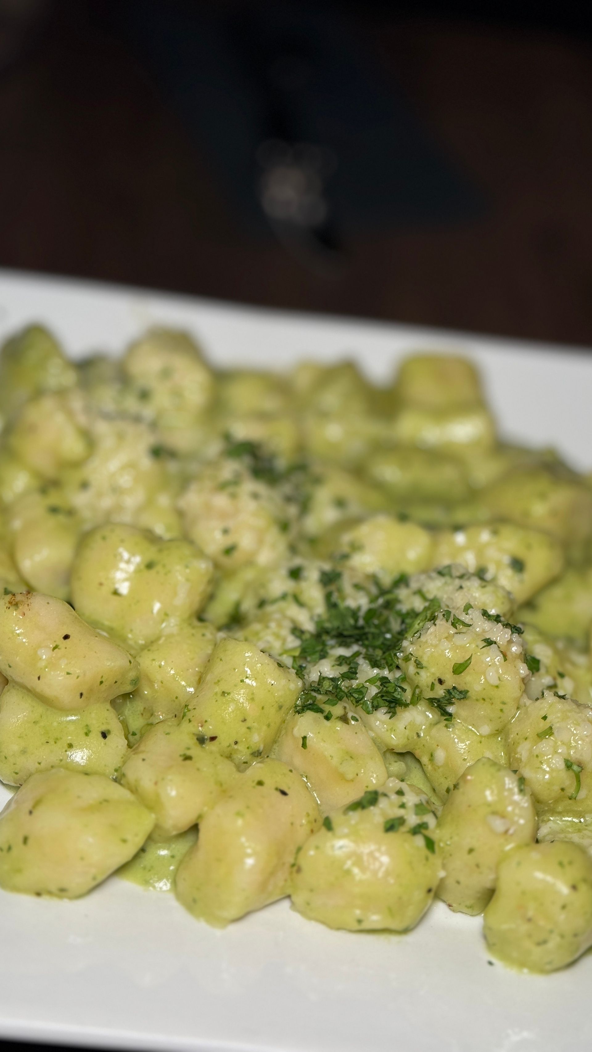 A white plate topped with gnocchi in a green sauce.