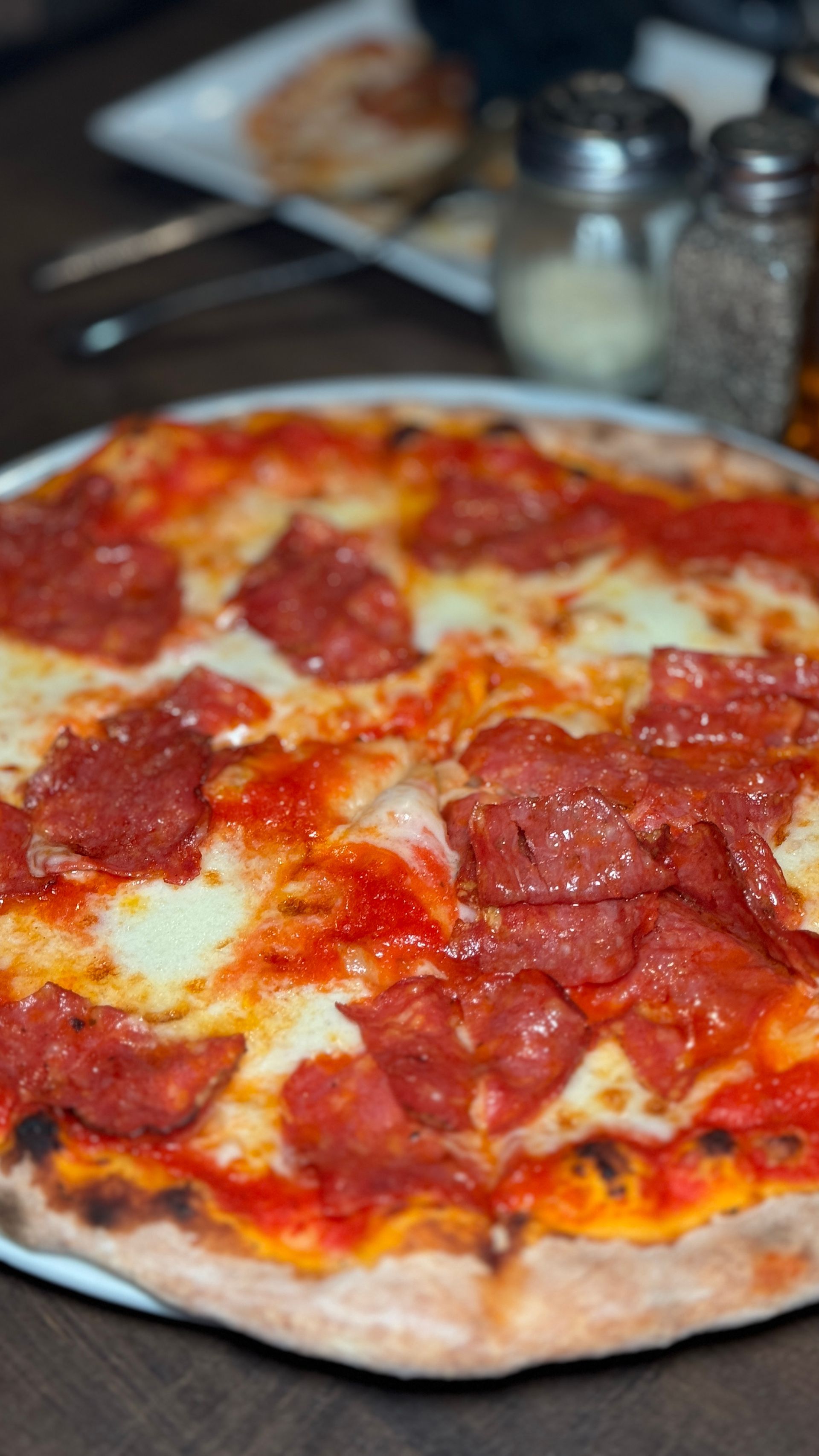 A pepperoni pizza is sitting on a white plate on a wooden table.