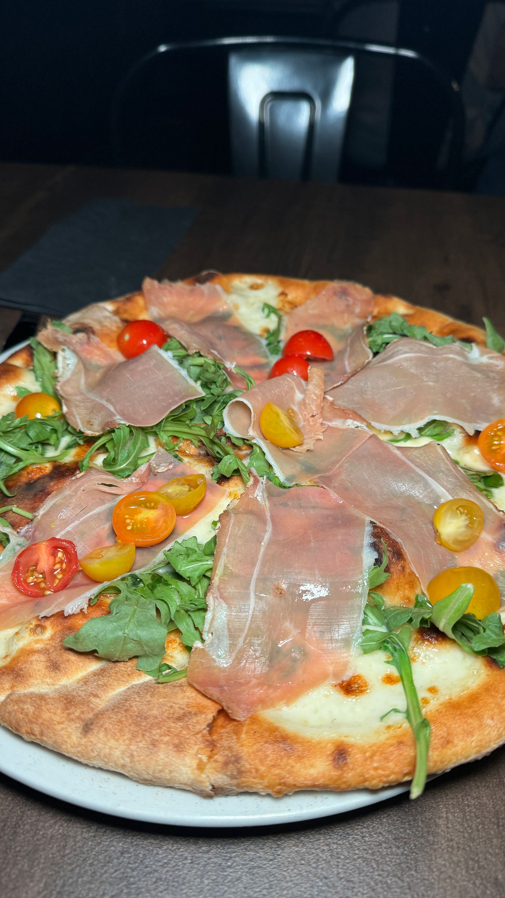 A pizza with ham and tomatoes on a white plate on a table.
