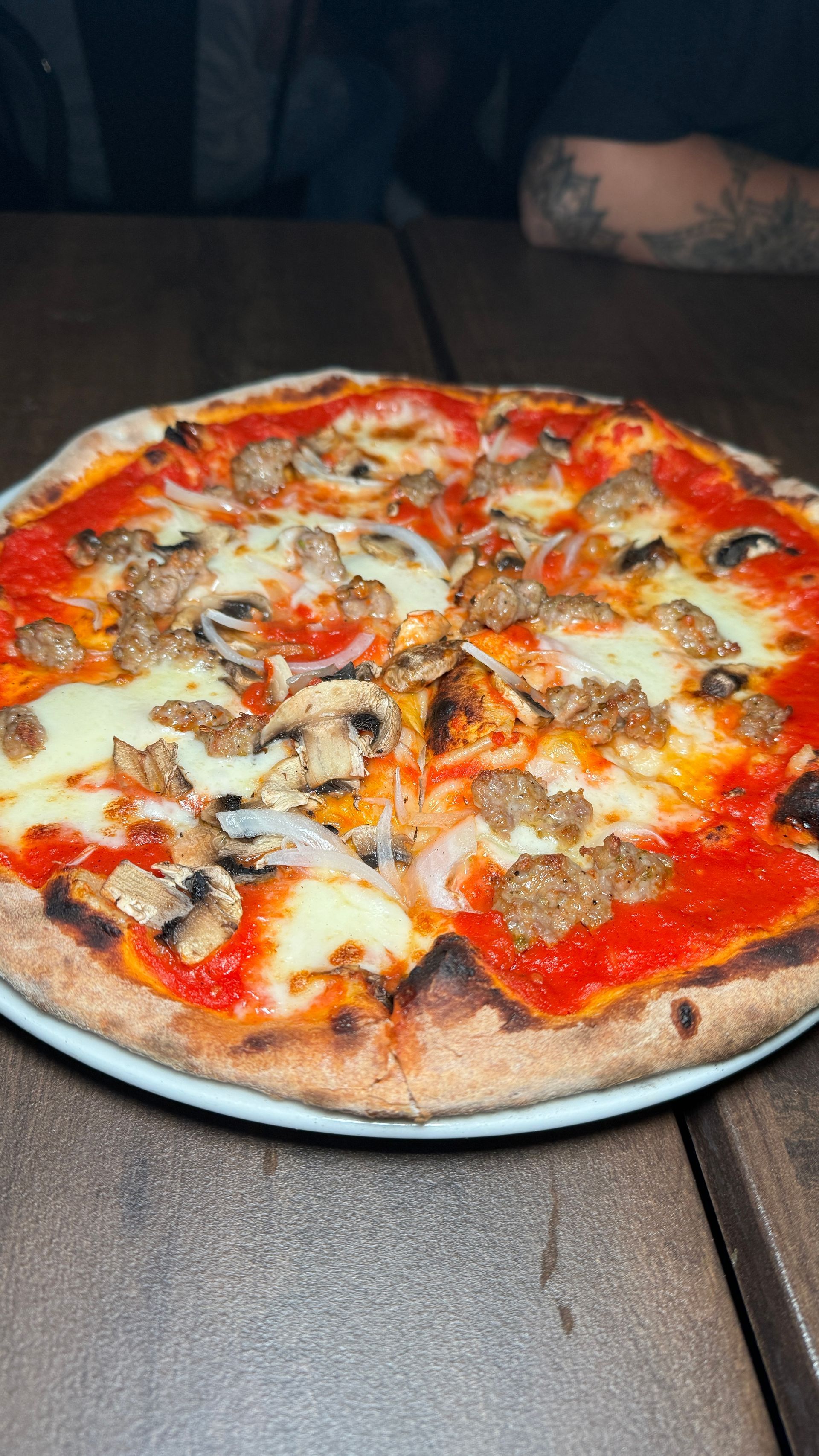 A pizza is sitting on a plate on a wooden table.