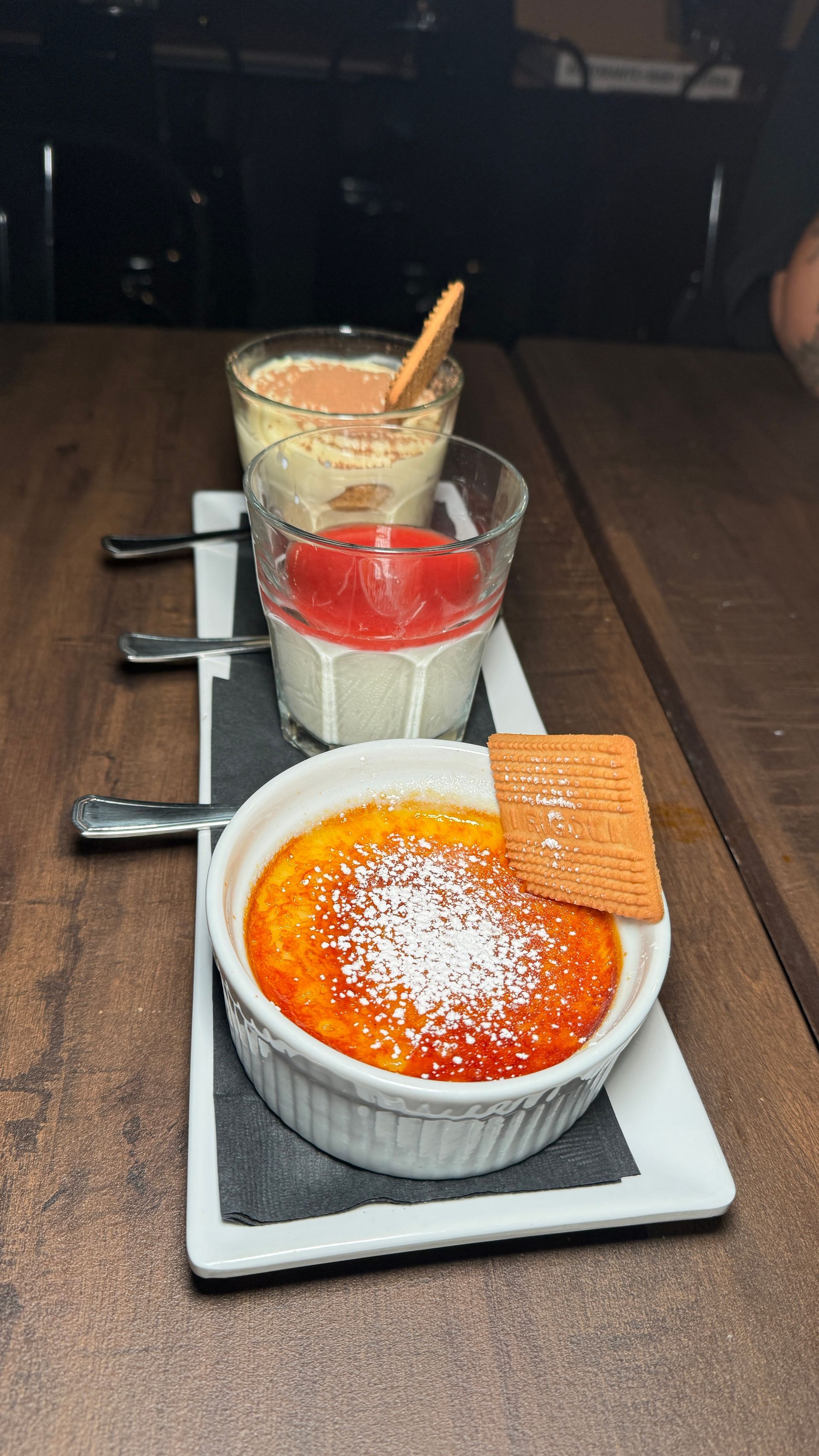 Three desserts are on a white plate on a wooden table.