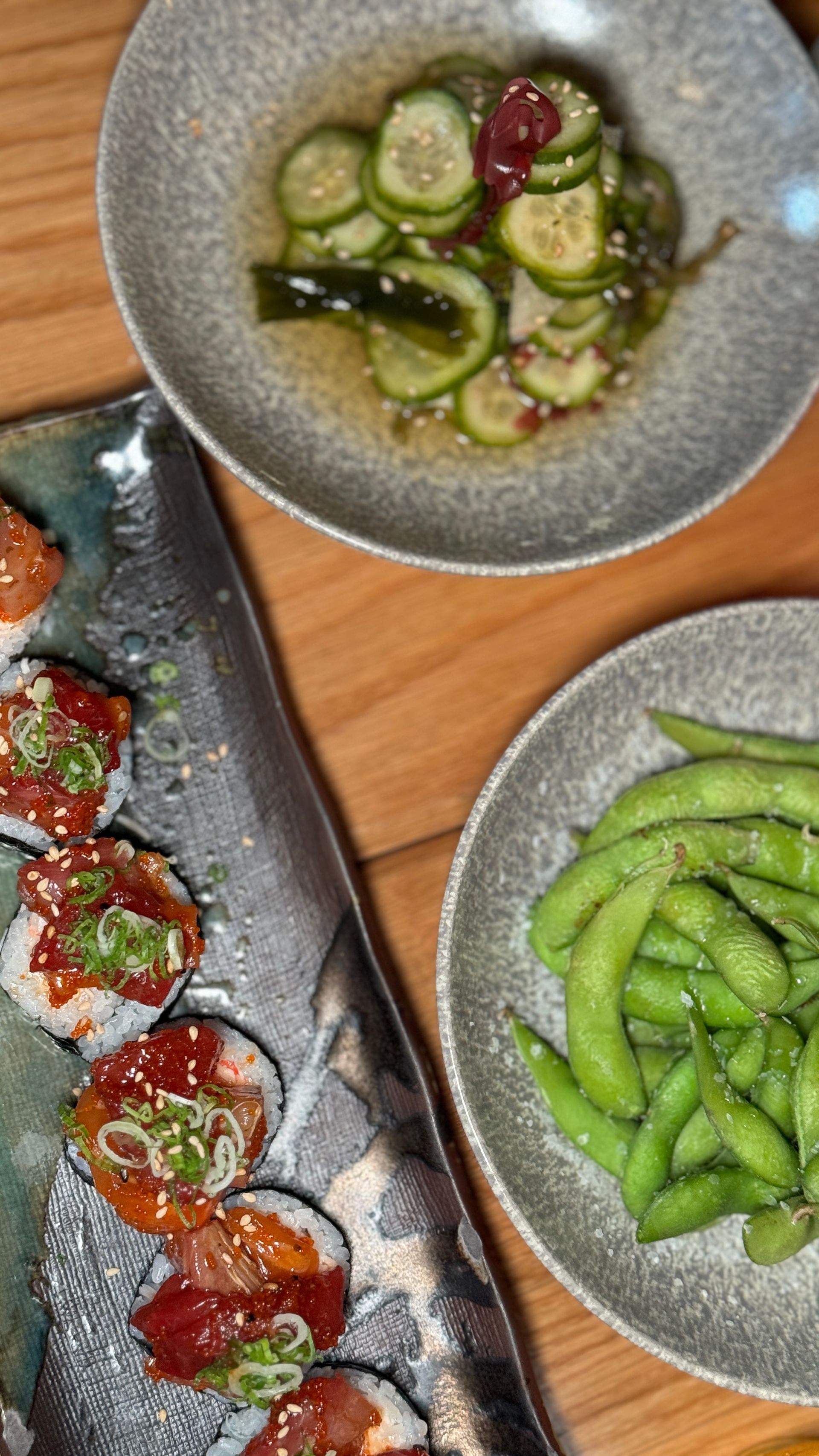There are three plates of food on the table , including sushi and edamame.