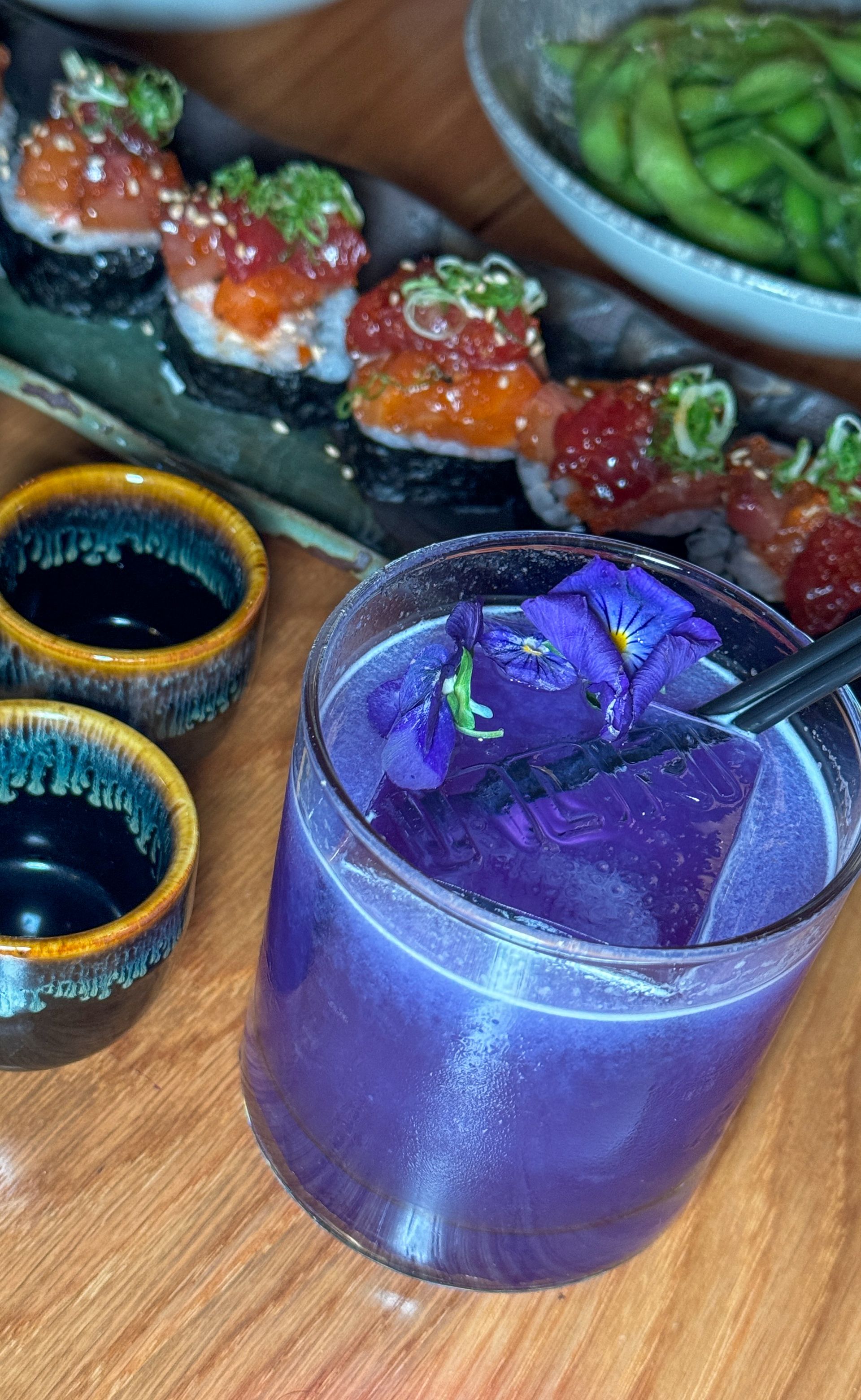 A purple drink is sitting on a wooden table next to sushi.