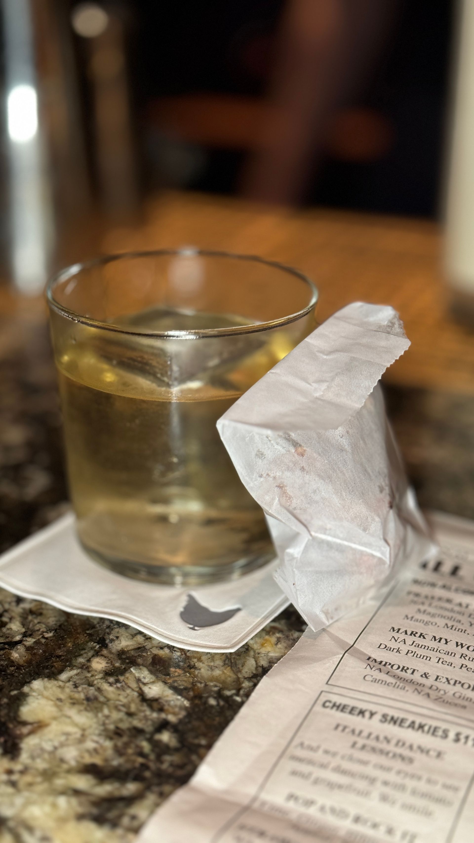 A glass of liquid is sitting on a napkin on a table next to a menu.