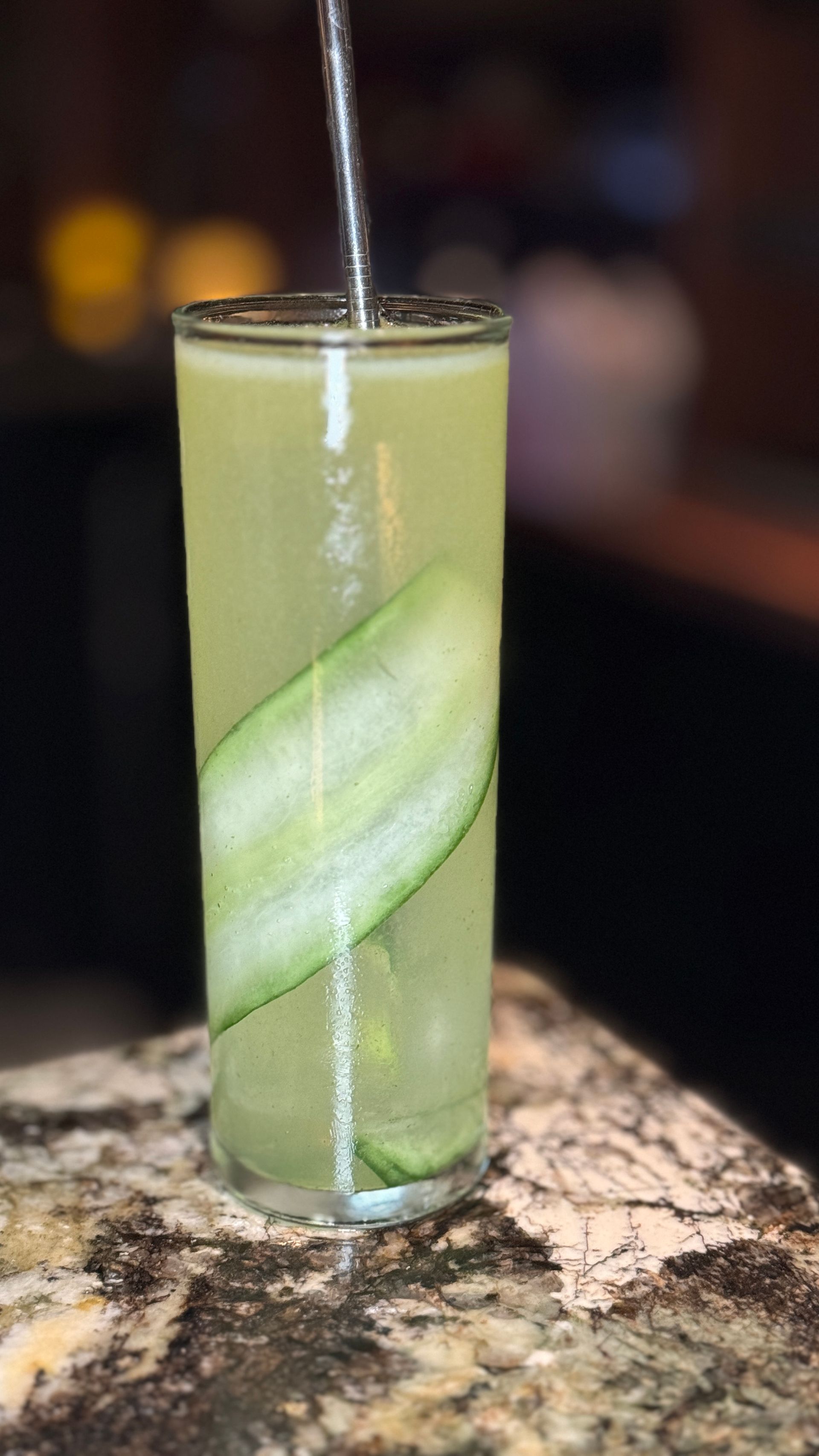 A tall glass filled with a green liquid and a cucumber slice.