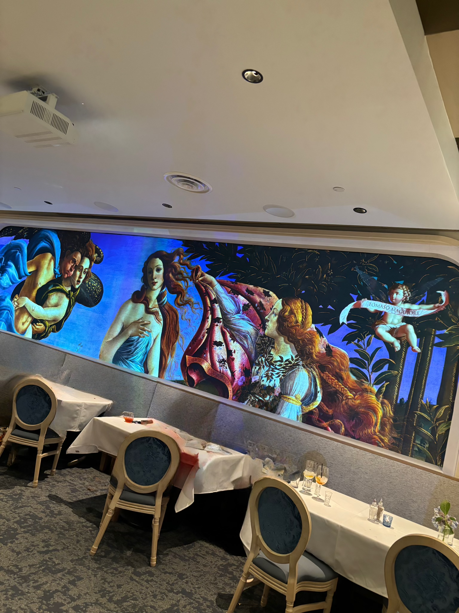 A restaurant with tables and chairs and a large painting on the wall.