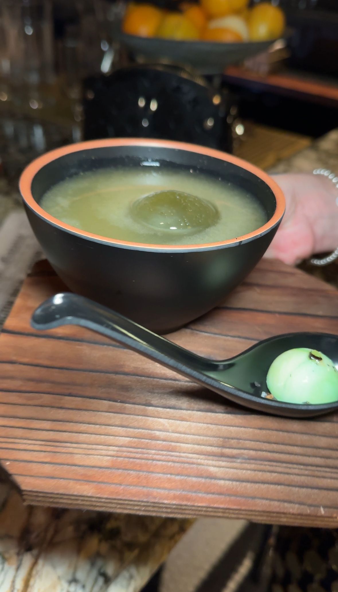 A bowl of soup and a spoon on a wooden table.