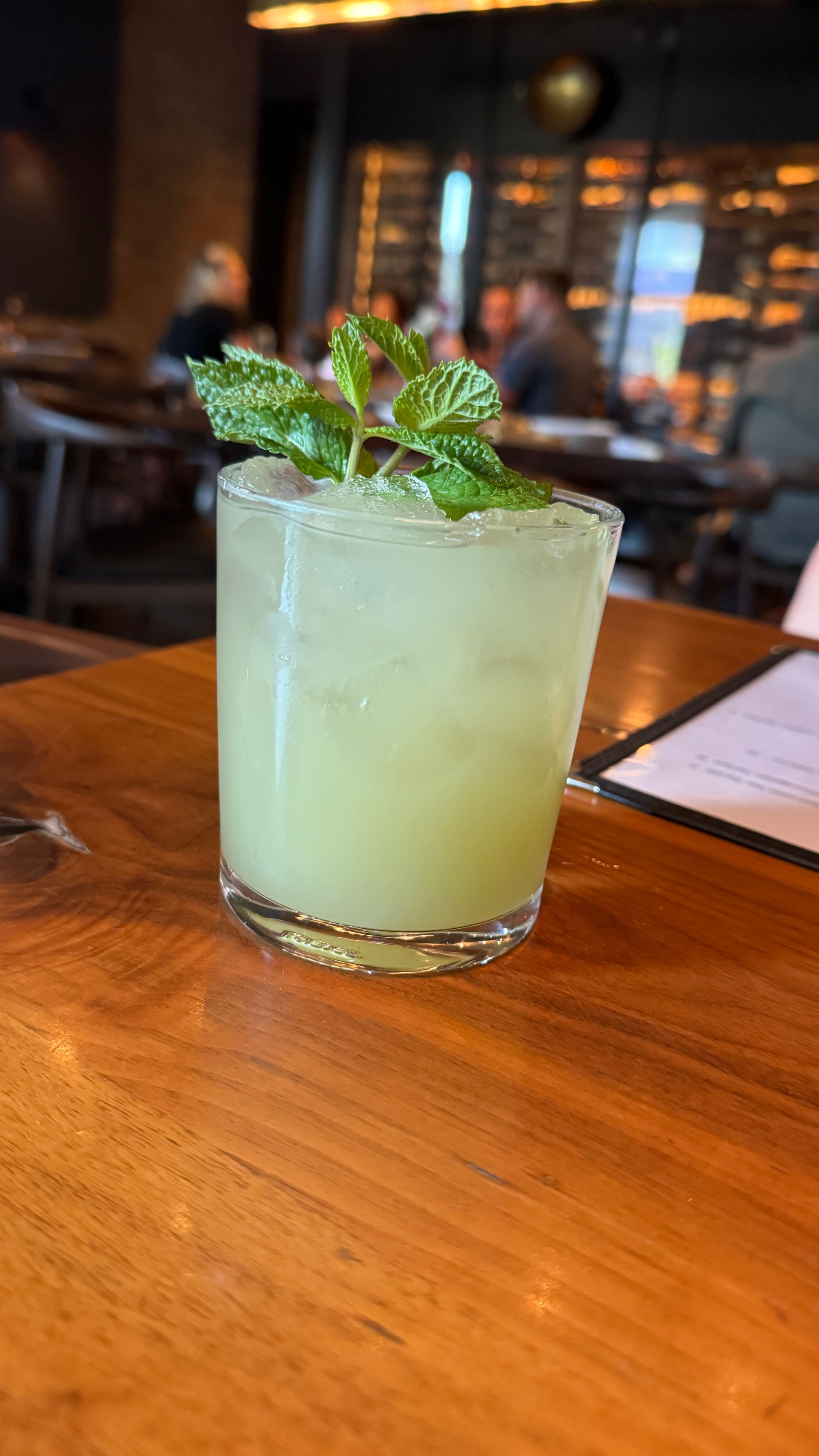 A green drink with mint leaves on top of it is on a wooden table.