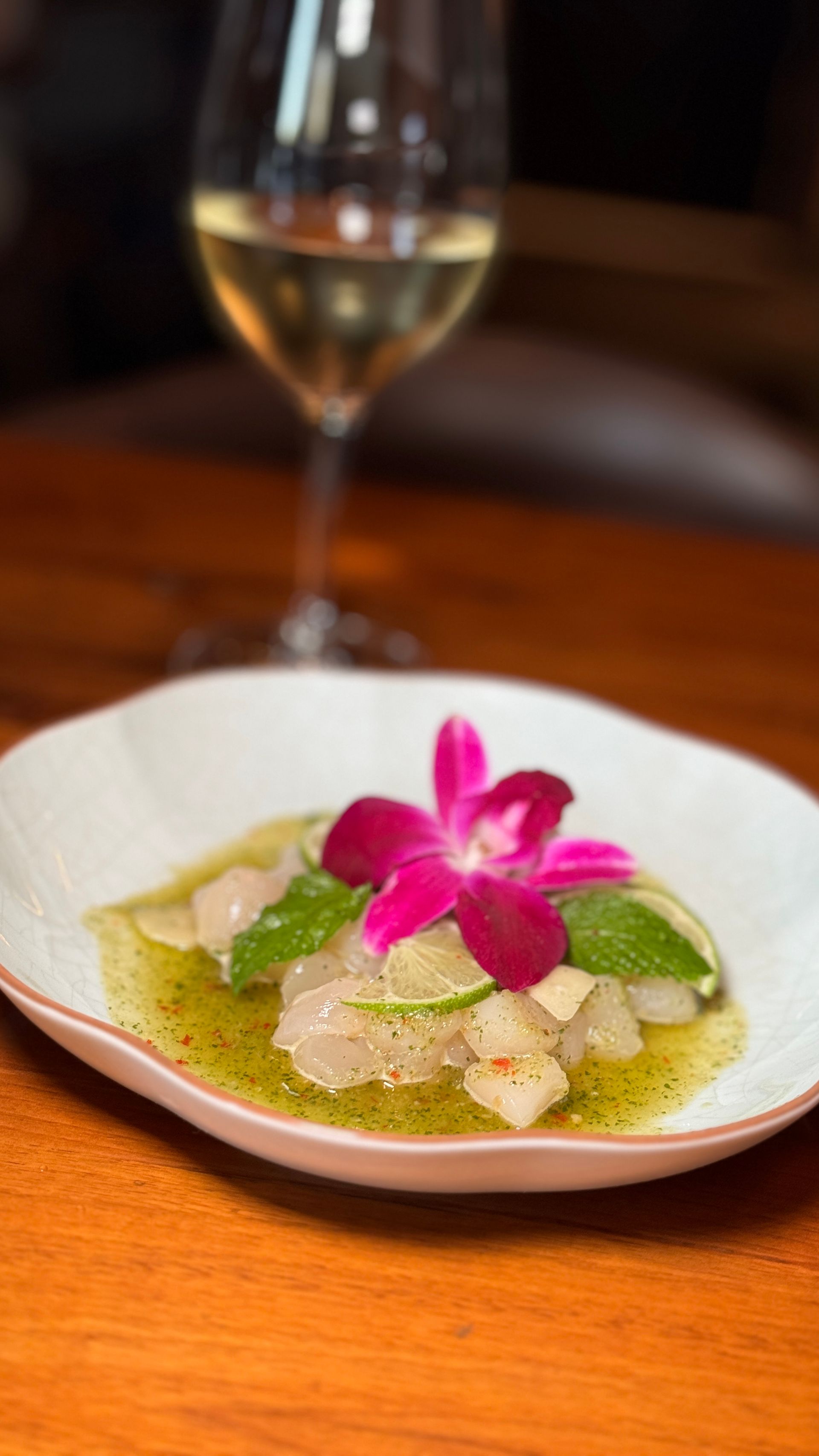 A plate of food with a flower on it and a glass of wine on a wooden table.
