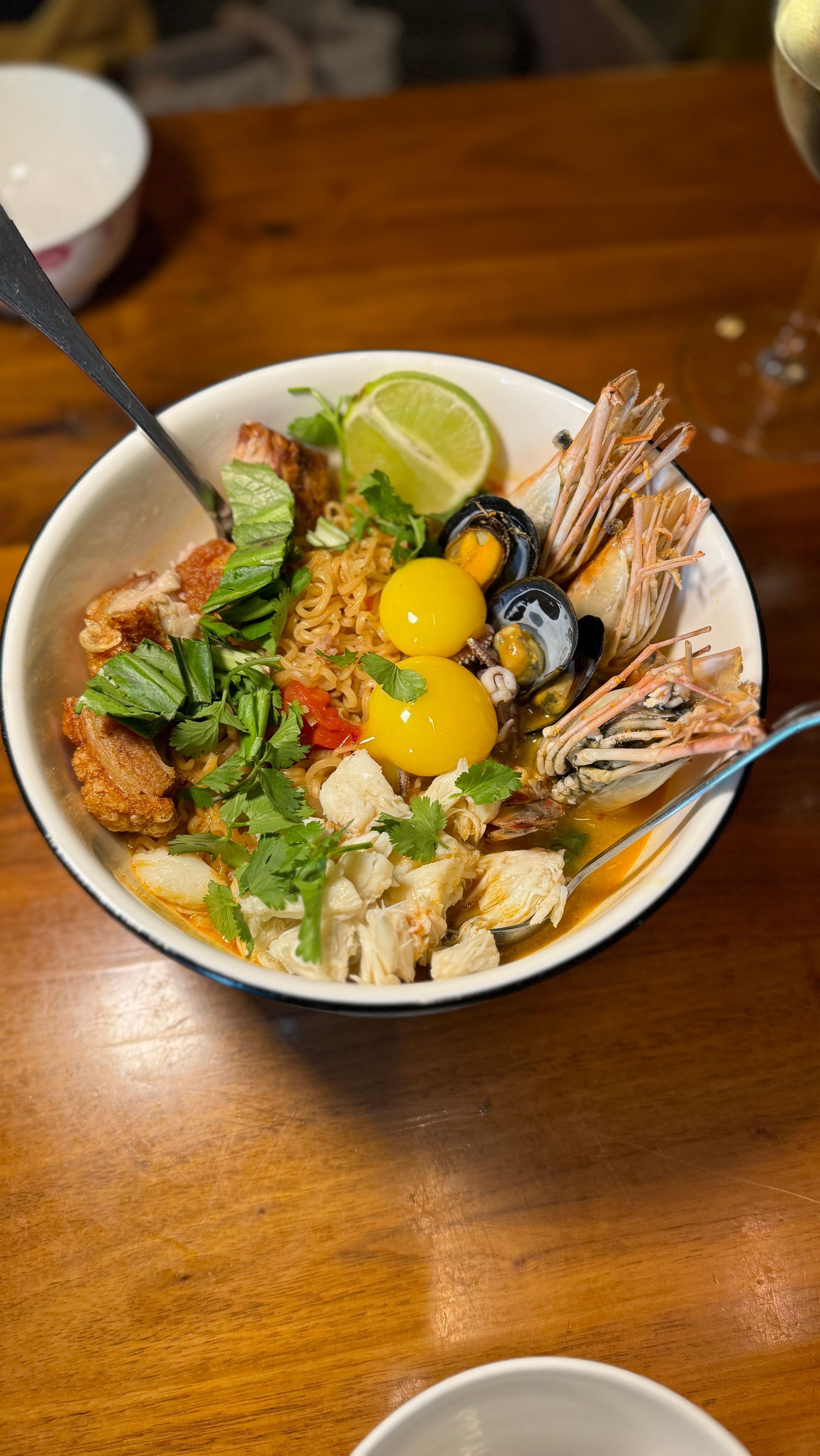 A bowl of food with a spoon in it is on a wooden table.