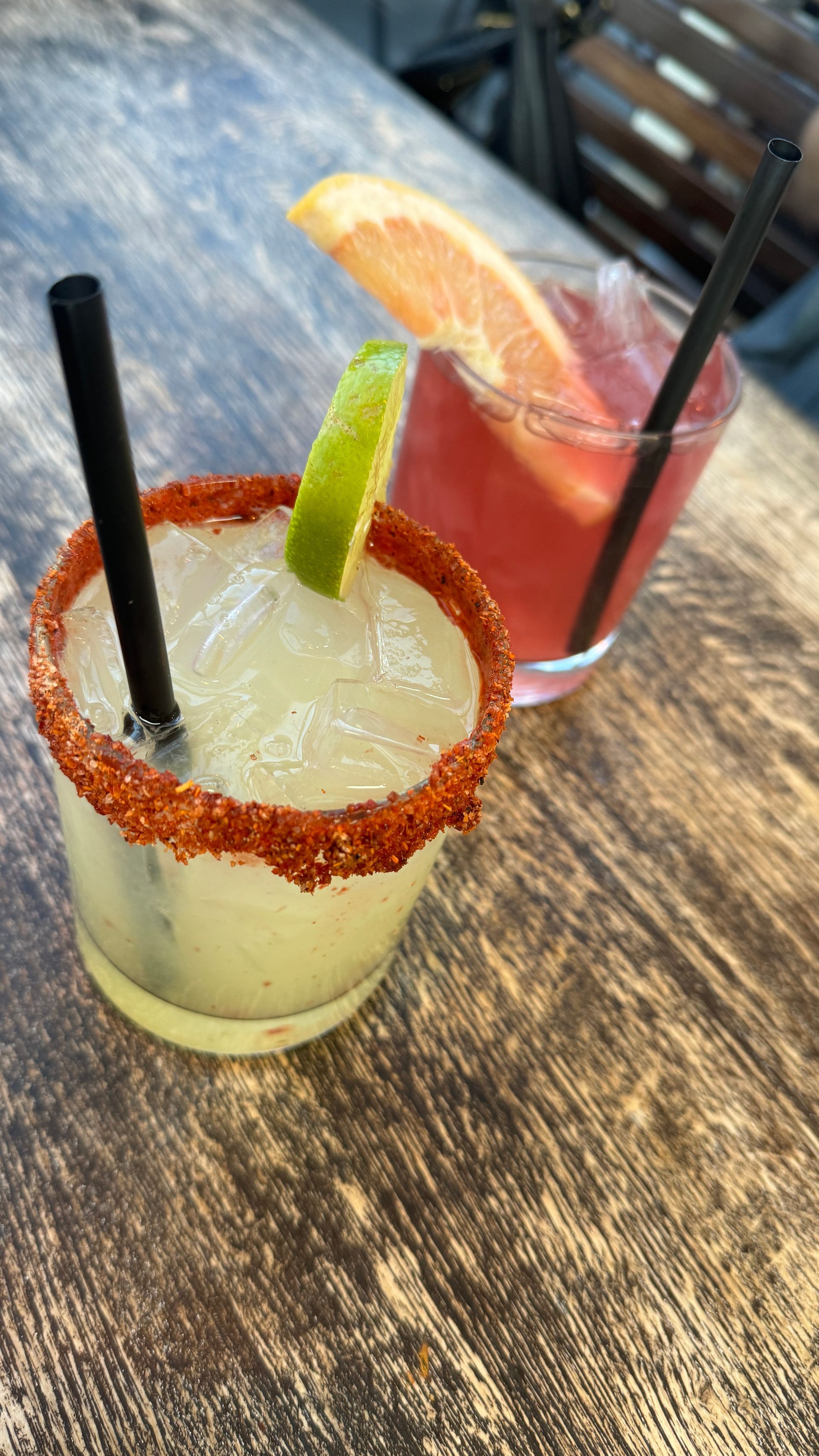 Two margaritas with straws on a wooden table.