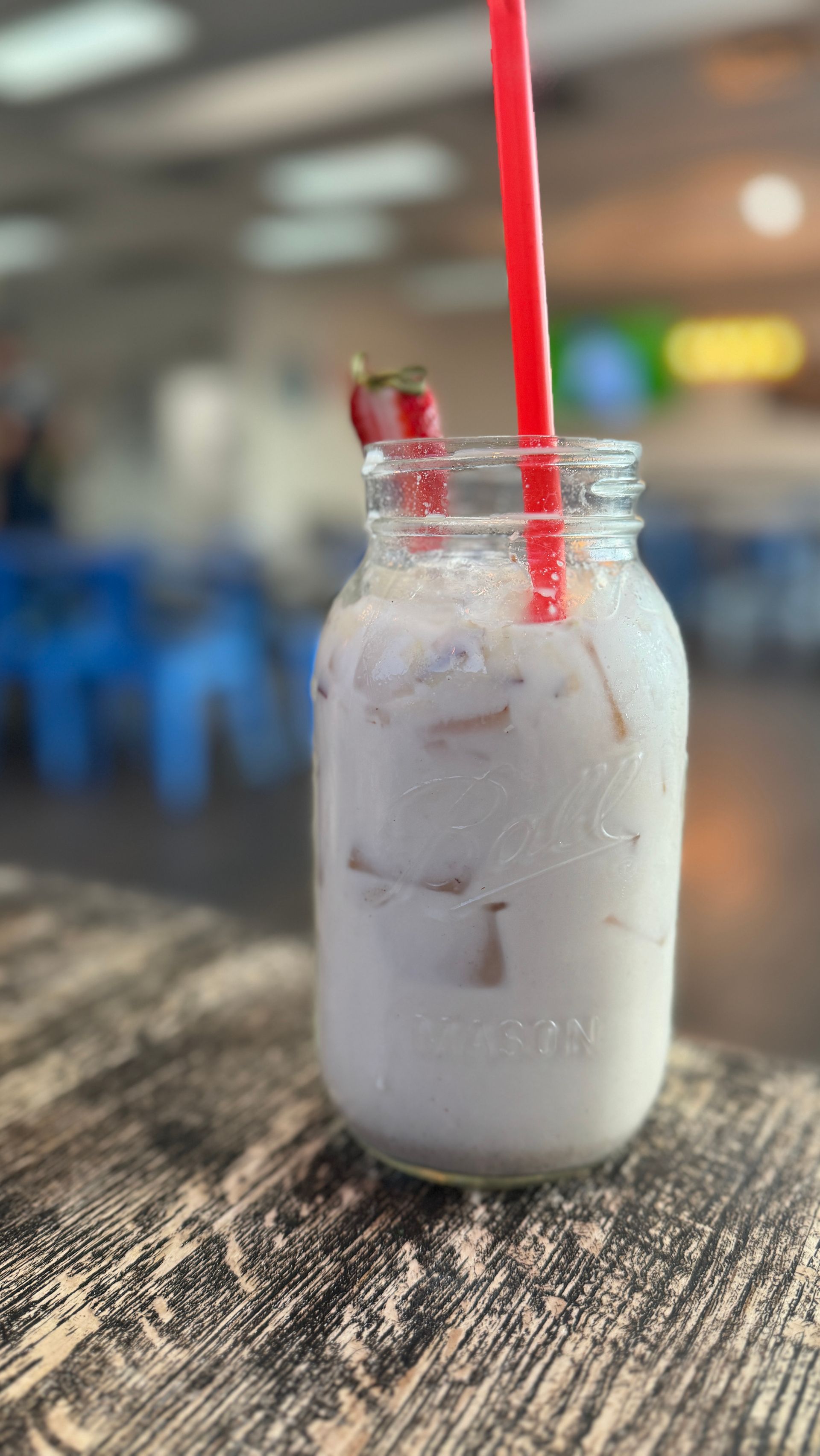 A jar of horchata with a red straw on a wooden table.