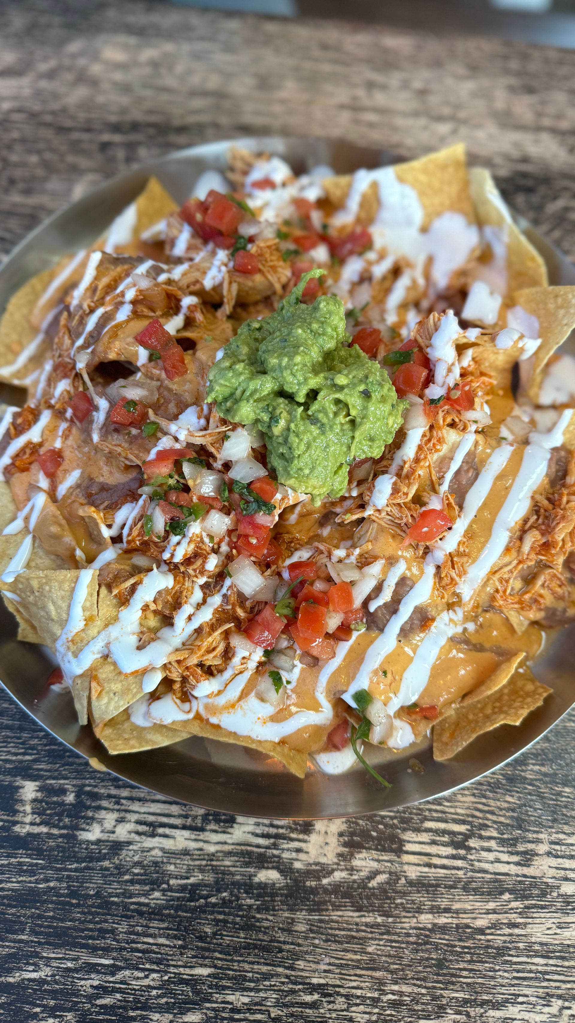 A close up of a plate of nachos on a wooden table.