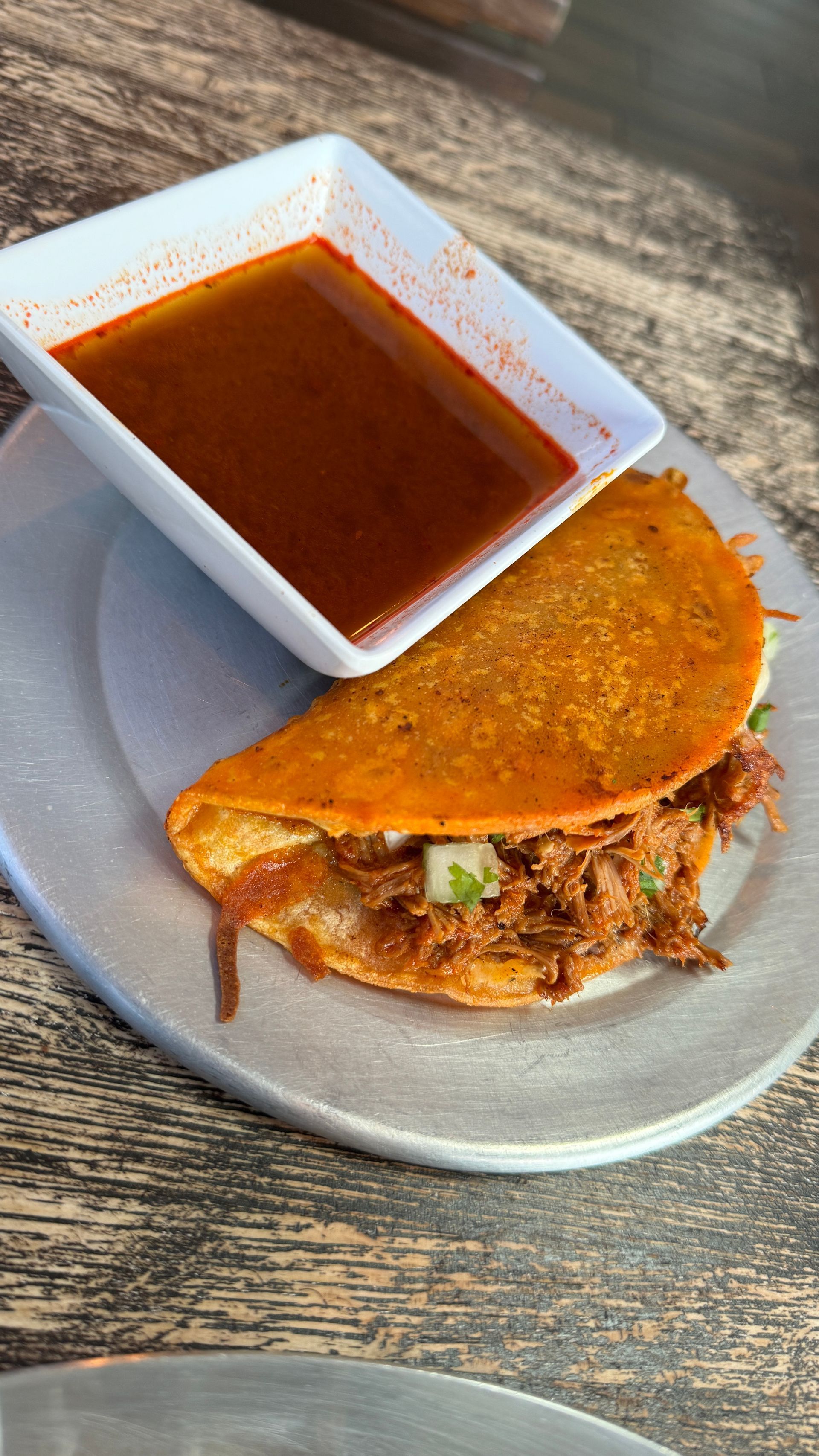 A taco is on a plate next to a bowl of sauce.