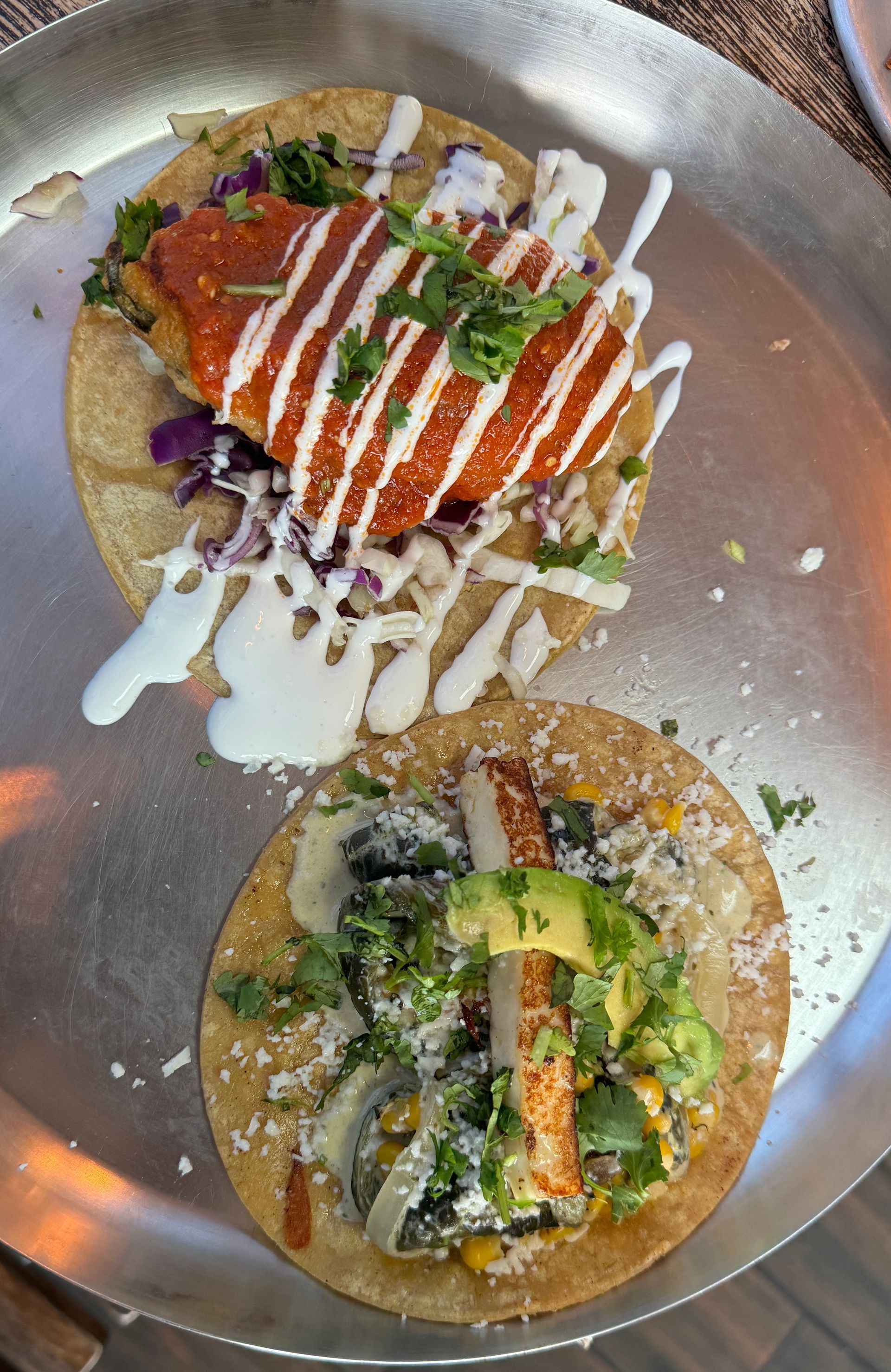 Two tacos are sitting on a metal tray on a table.