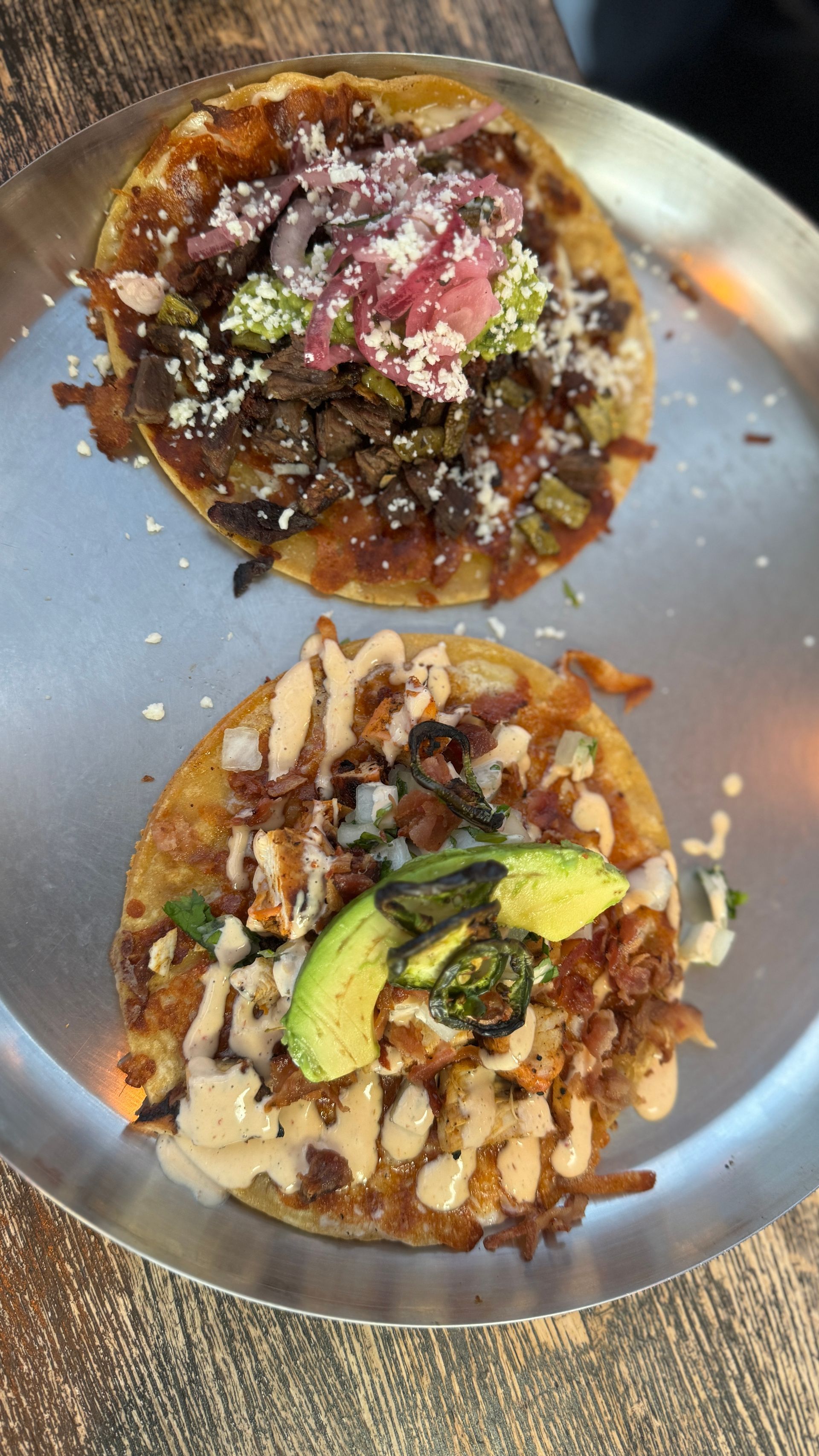 Two tacos are sitting on a metal plate on a wooden table.