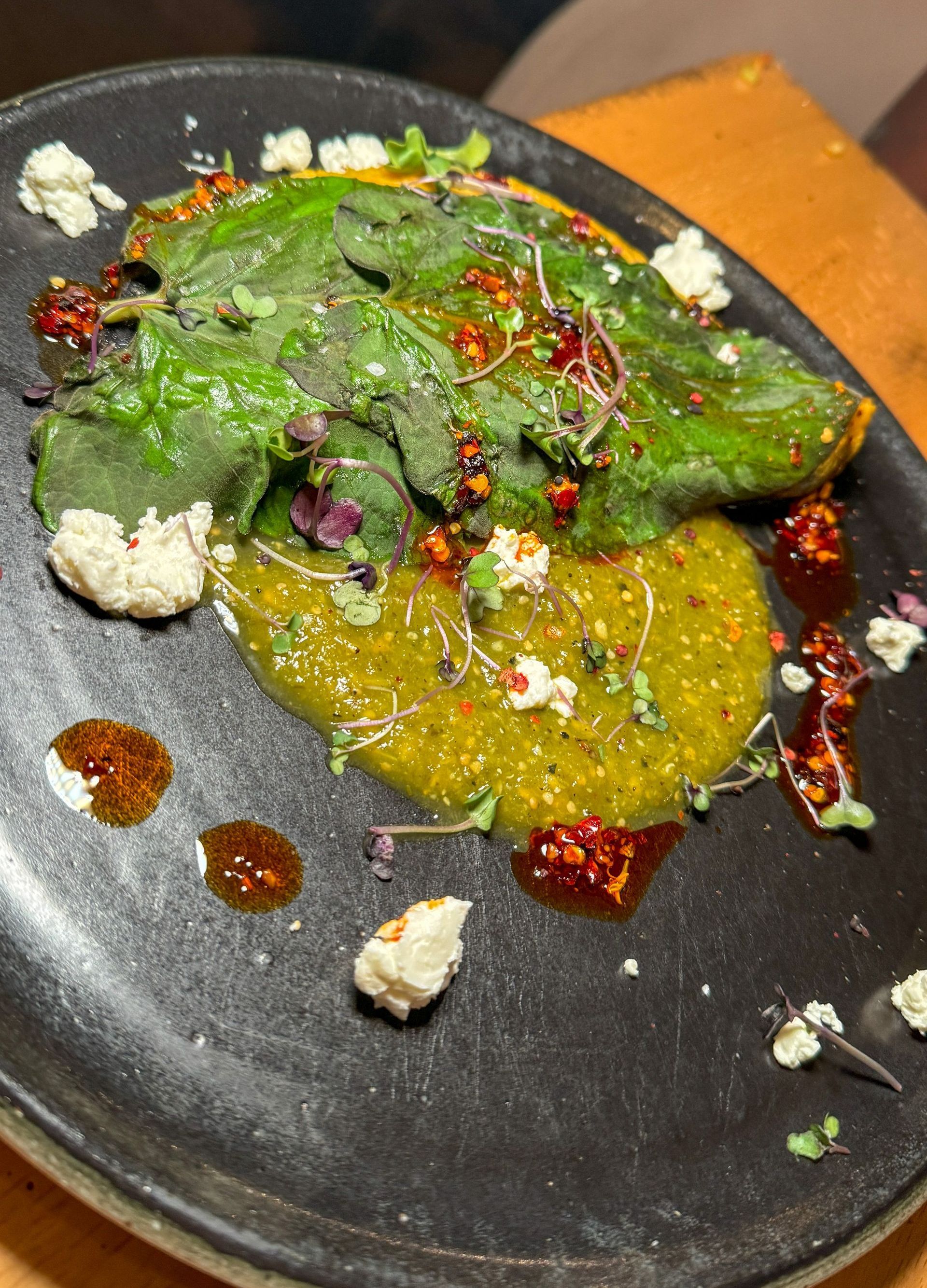 A black plate topped with a salad and sauce on a wooden table.