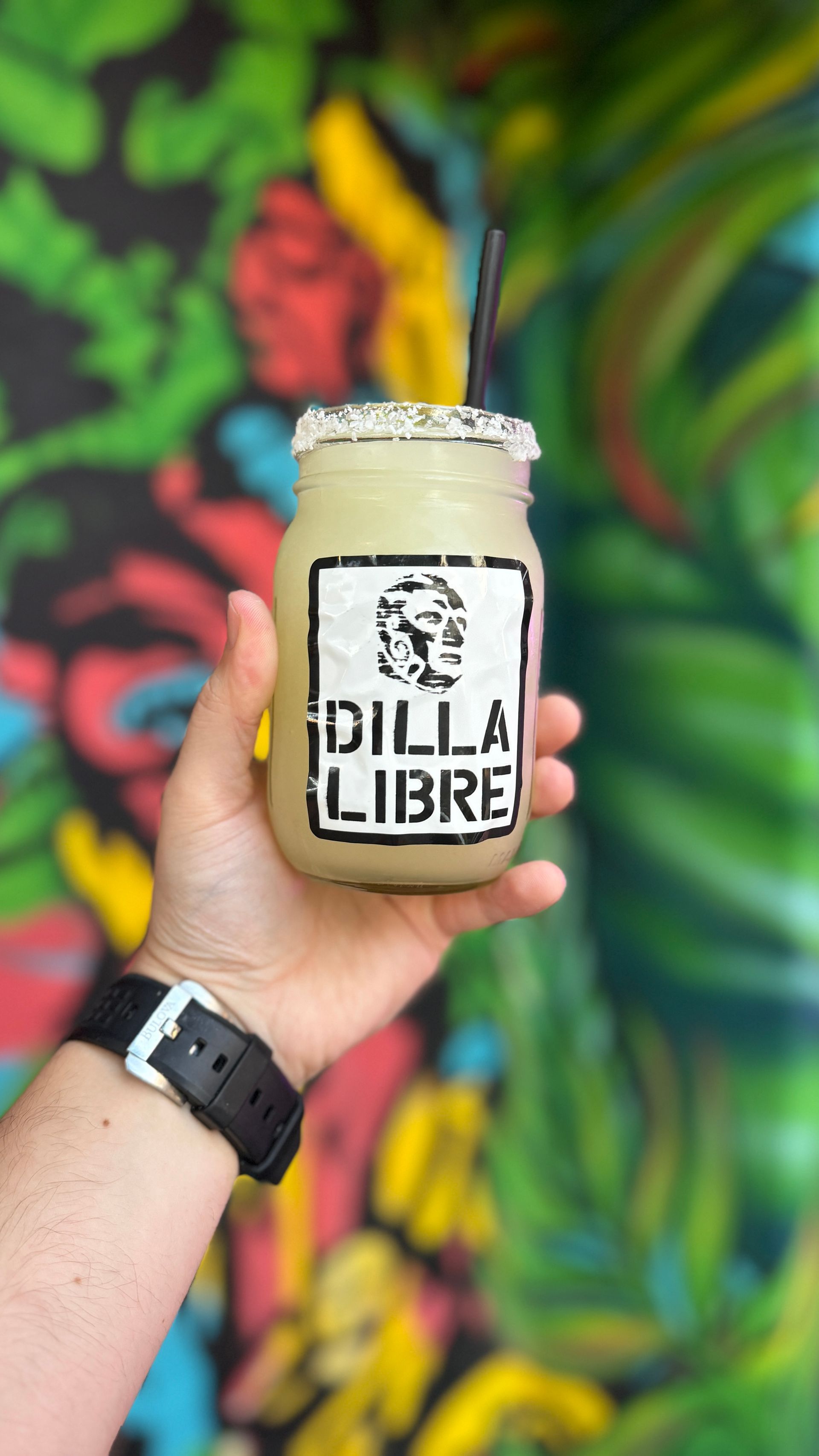 A person is holding a drink in a mason jar with a straw.