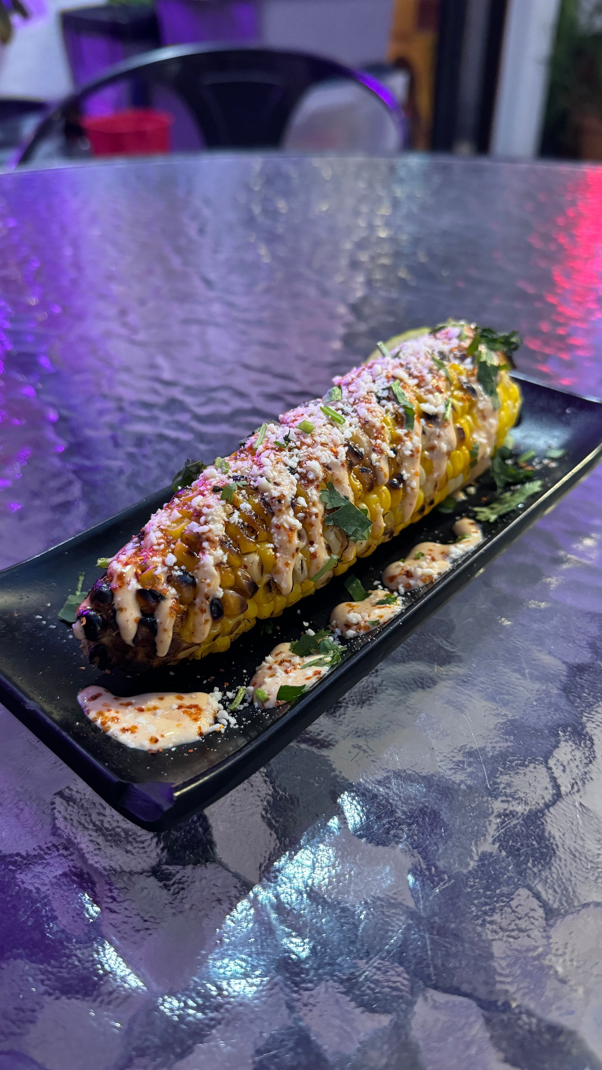 A close up of a corn on the cob on a black plate on a table.