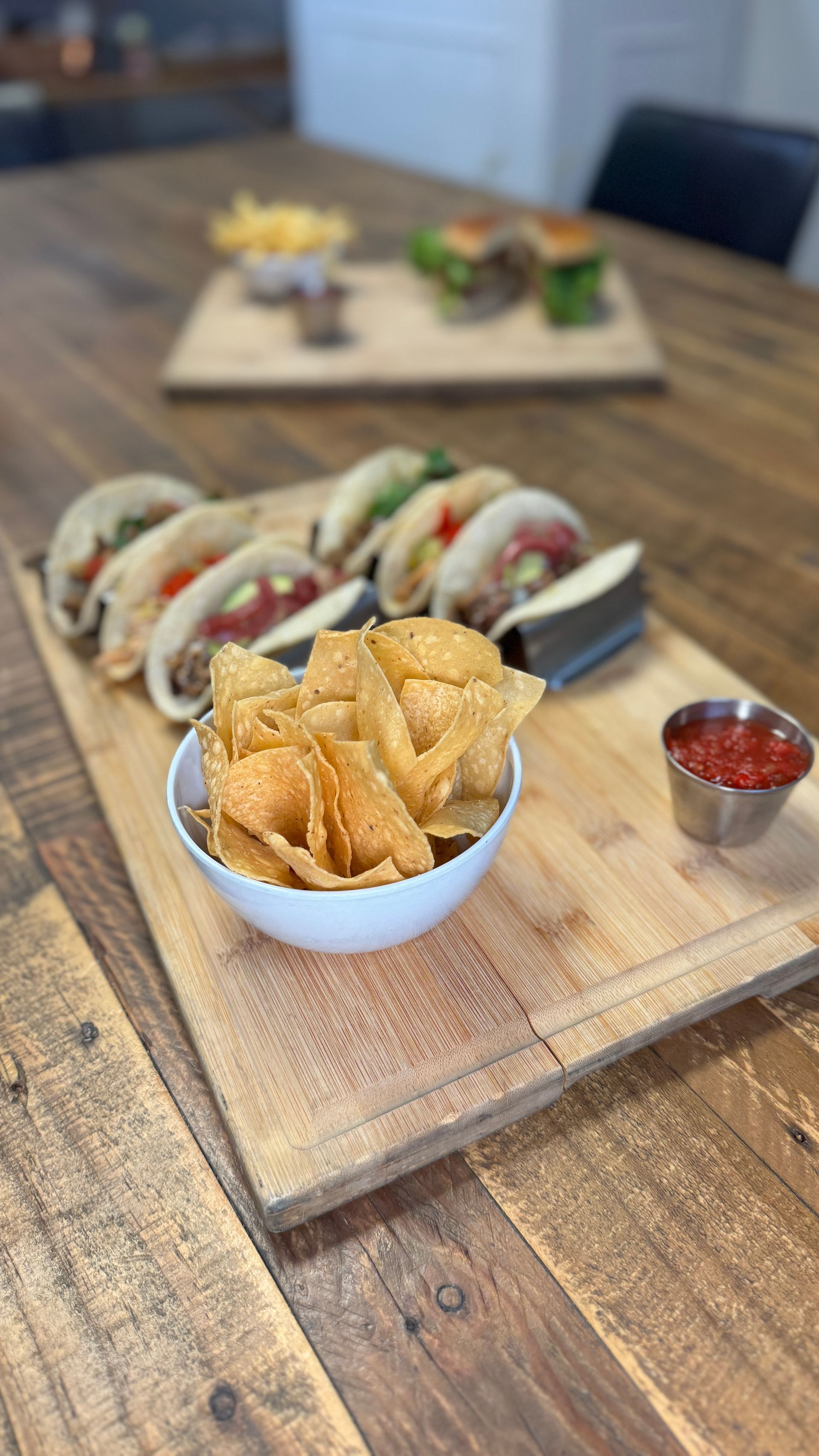 A wooden cutting board topped with tacos and tortilla chips.