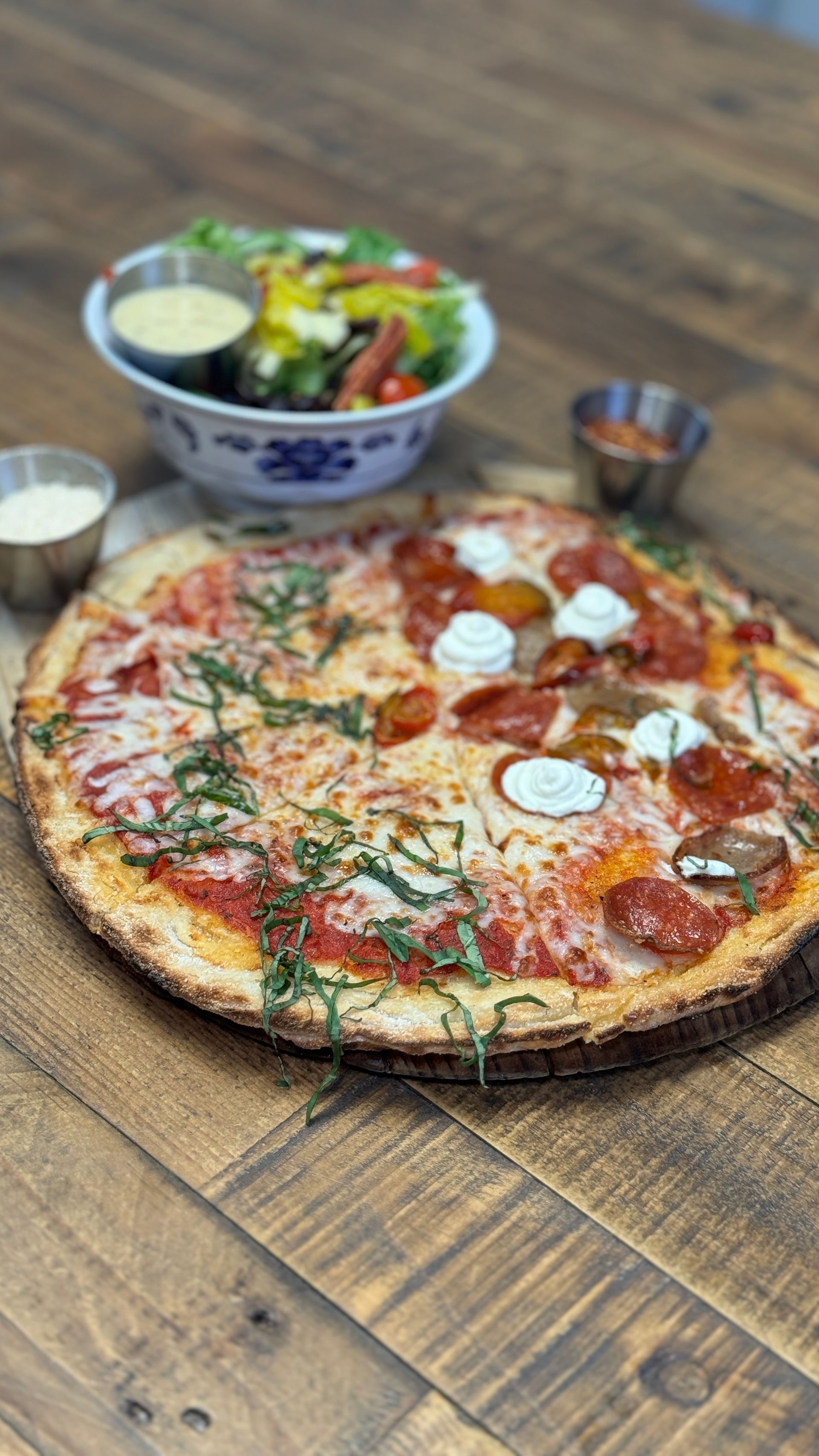 A pizza and a salad are on a wooden table.