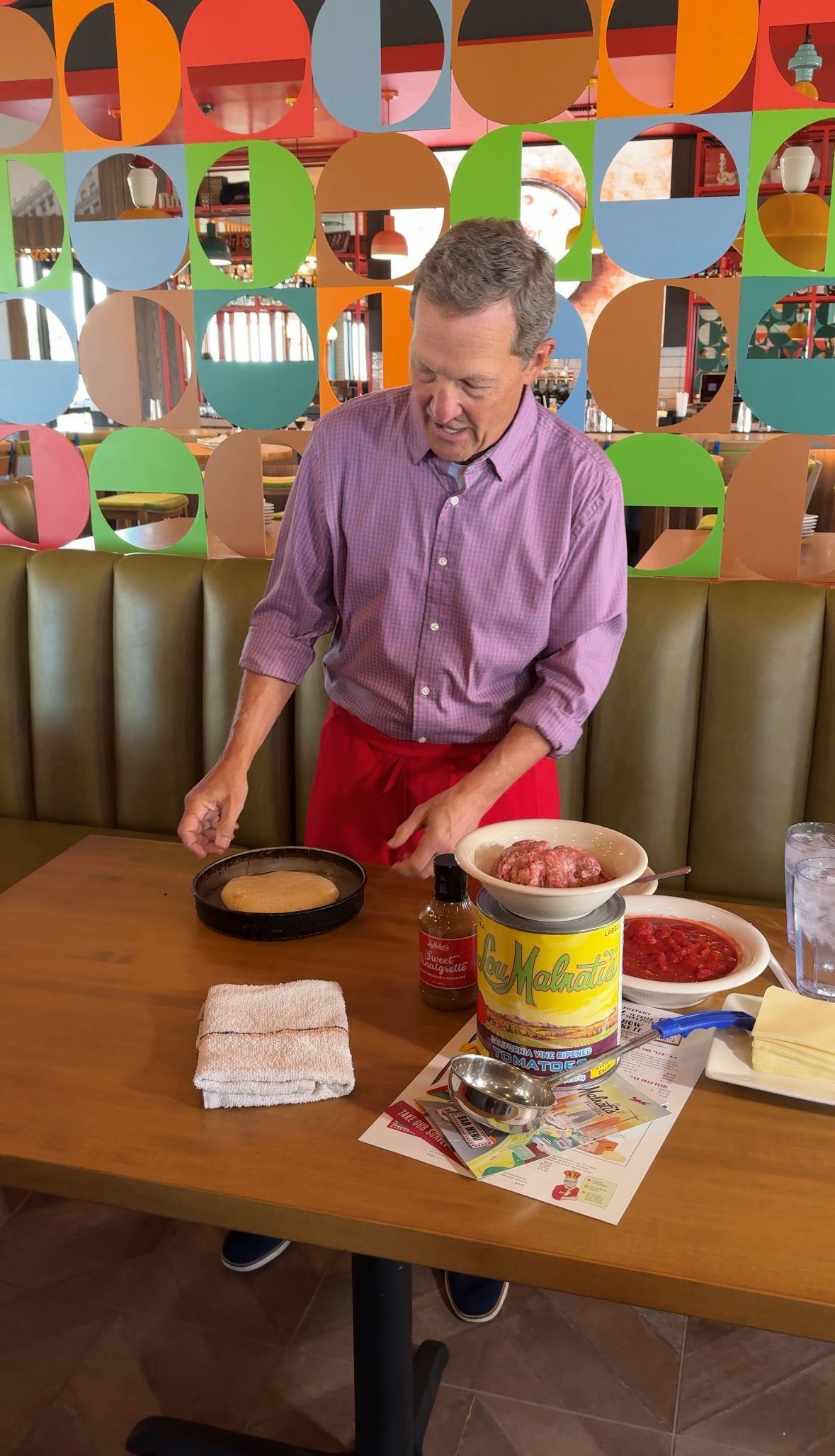 Marc Malnati is standing at a table in a restaurant preparing pizza.