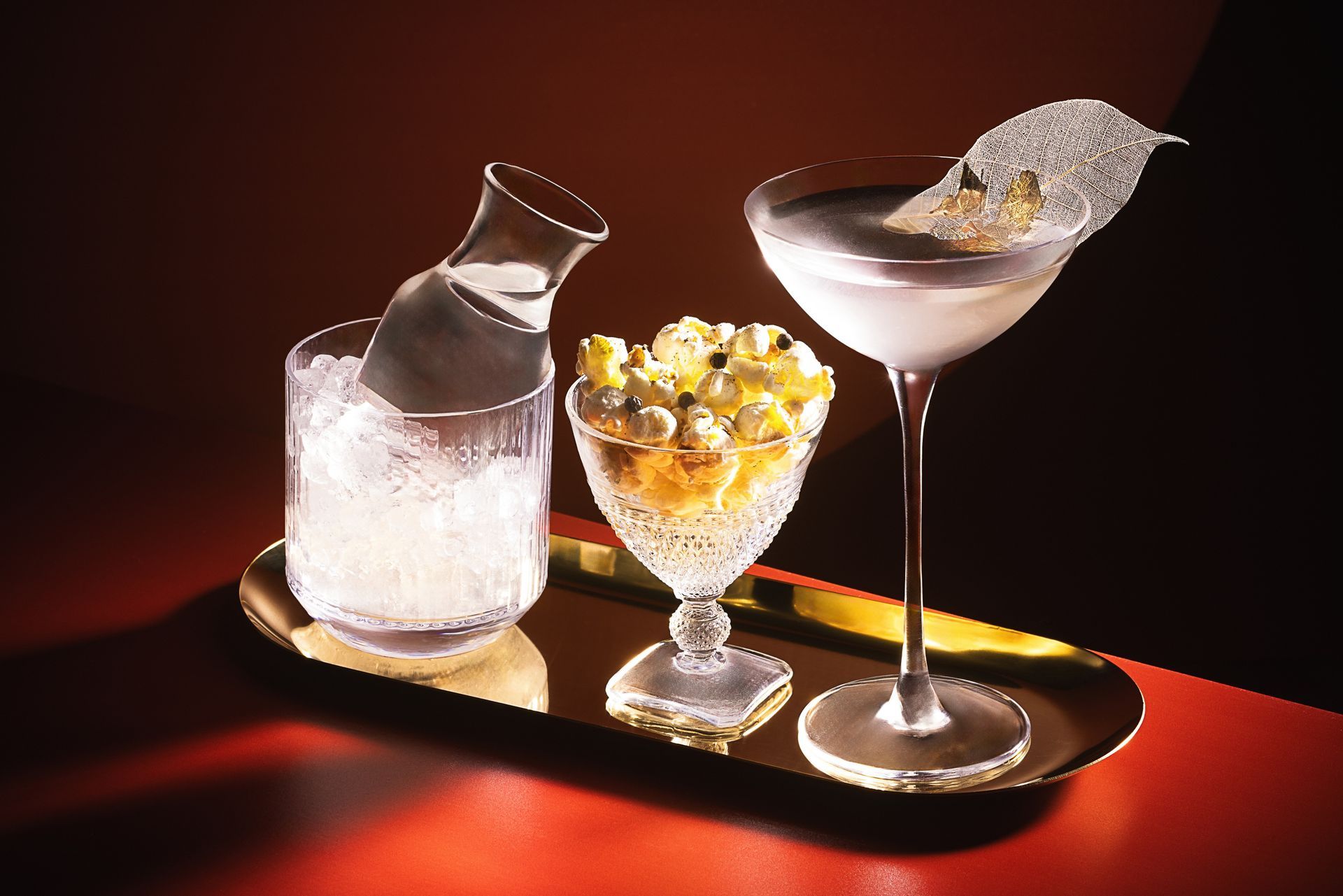 A tray with a martini , a pitcher and a bowl of popcorn on it.