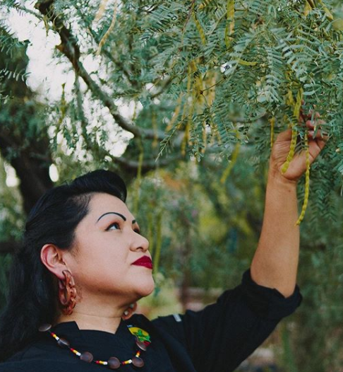 A woman is reaching up to a tree branch