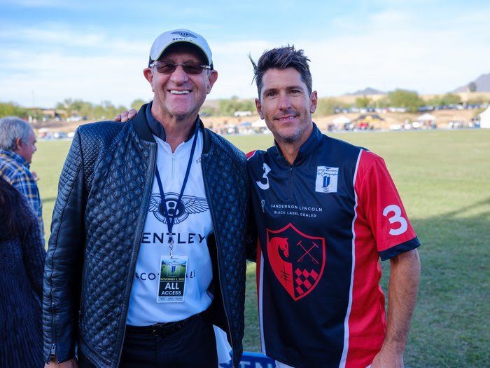 Two men are posing for a picture on a field . one of the men is wearing a bentley shirt.
