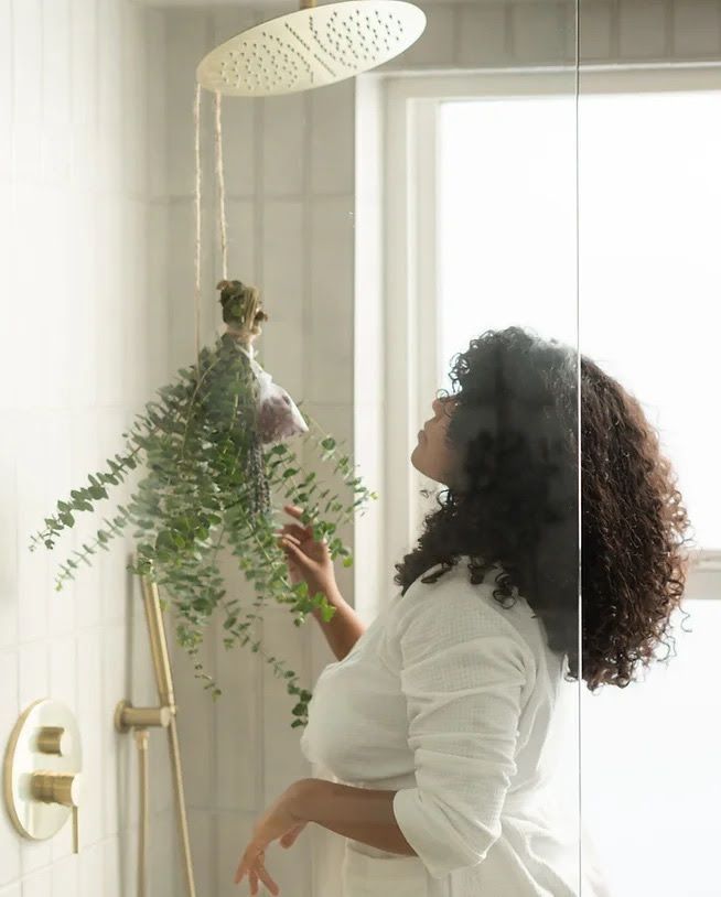 A woman is standing in a shower with a plant hanging from the shower head.