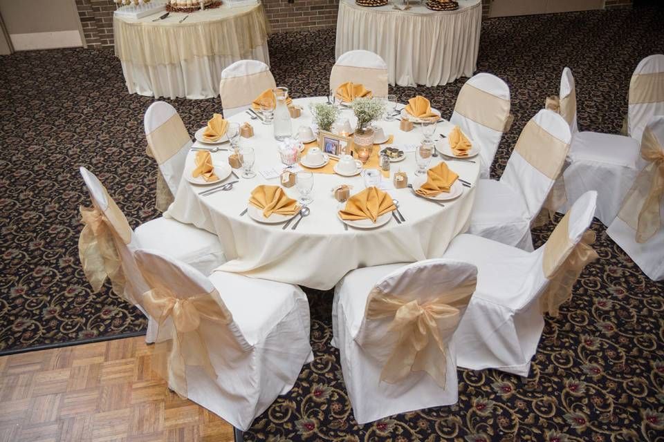 Red-lit banquet hall with round tables set with black and red tablecloths and chairs, ready for an event.