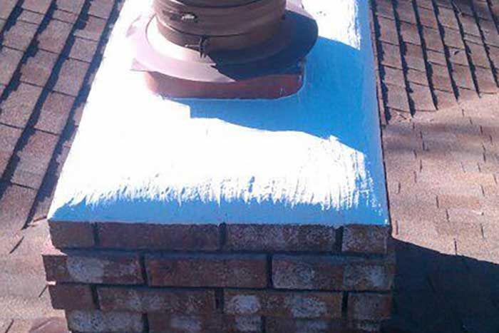 Brick chimney with white sealant on top, brown vent and asphalt roof.