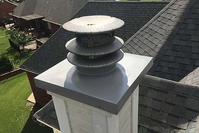 Chimney with silver cap and tiered vent on a gray shingle roof.