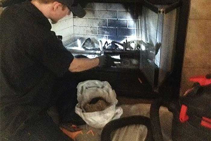 A person cleaning a fireplace, holding a bag of ashes.