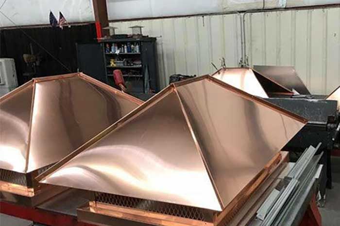 Copper chimney caps in a workshop, showcasing a pyramid design.