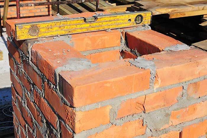 Brick chimney being built, with a level placed on top to ensure accuracy.