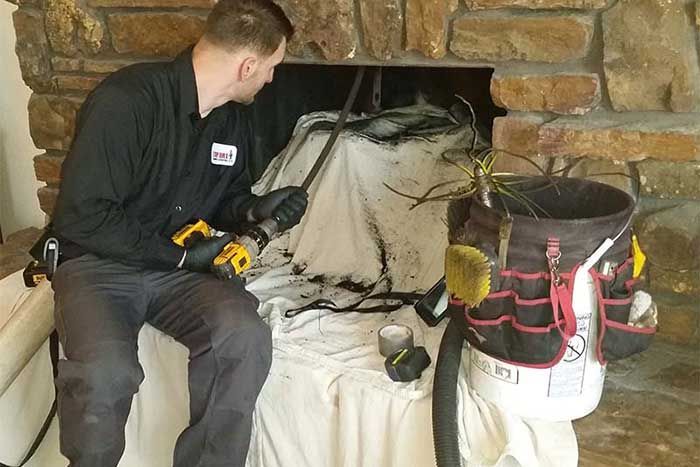 Man cleaning a fireplace with a drill and brush. A white drop cloth covers furniture.
