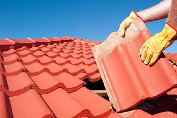 Person in yellow gloves installing a red tile on a roof.