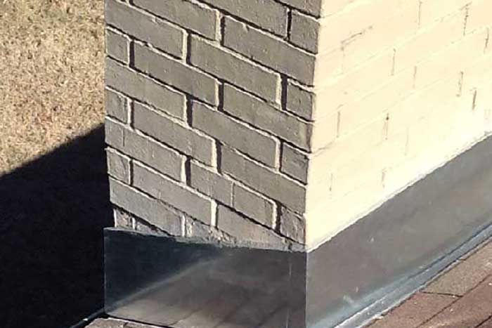 Corner of a brick chimney with angled brickwork, set on a roof with metal flashing.