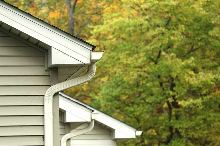 White house corner with gutters; fall foliage in background.