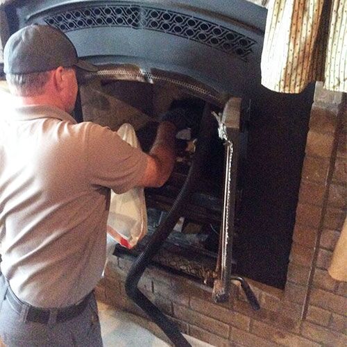 Man cleaning a fireplace with a vacuum hose.